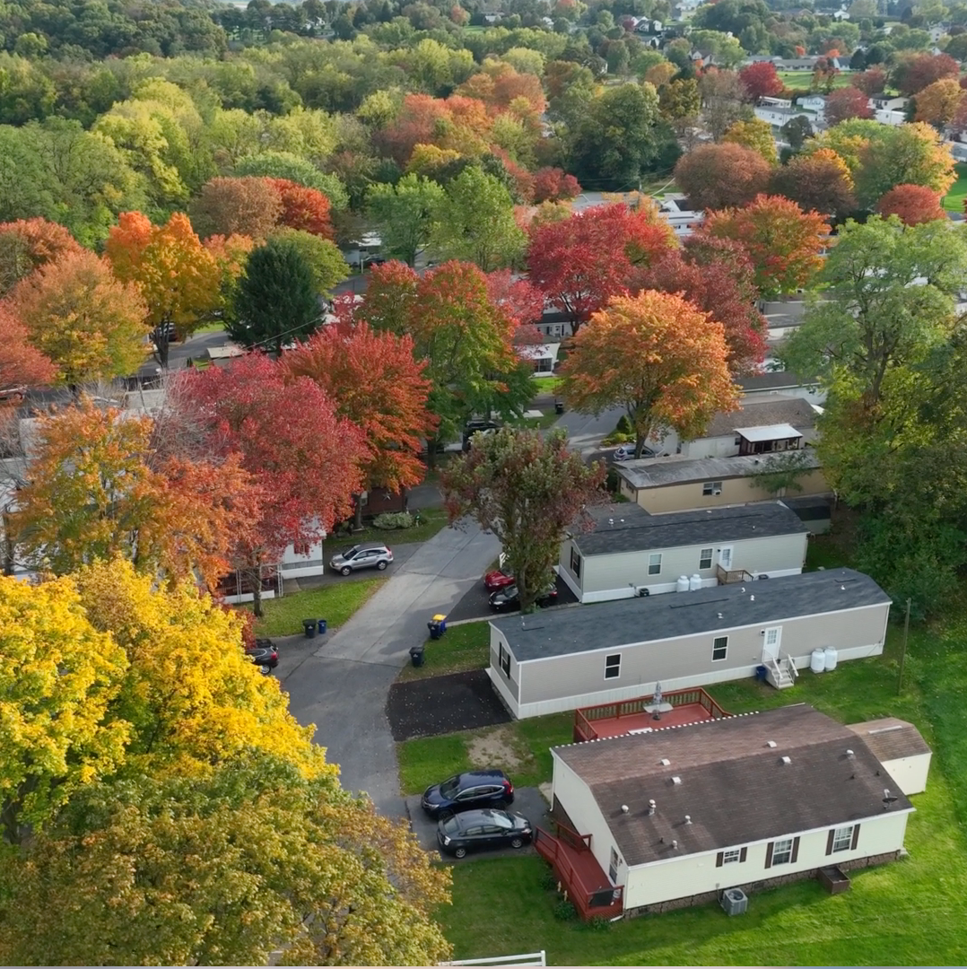 An aerial view of a neighborhood with a mix of homes and residential buildings surrounded by colorful fall trees with red, orange, yellow, and green foliage.