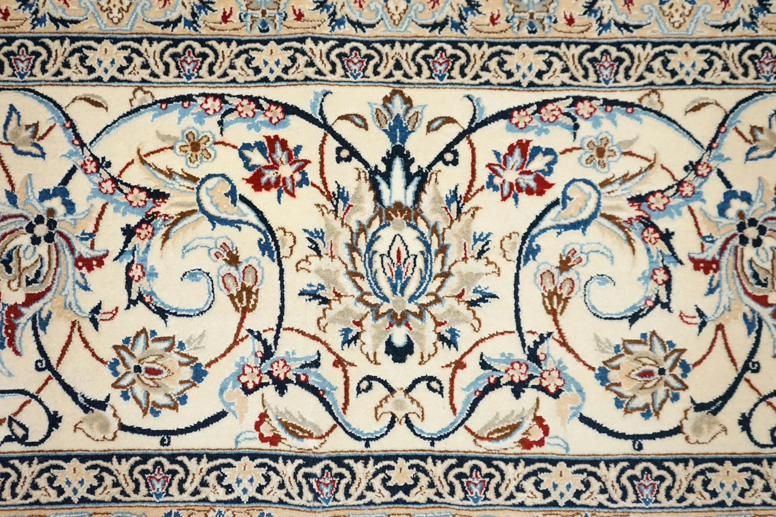 A patterned Persian-style rug with intricate floral designs in cream, navy blue, red, and light blue colors.