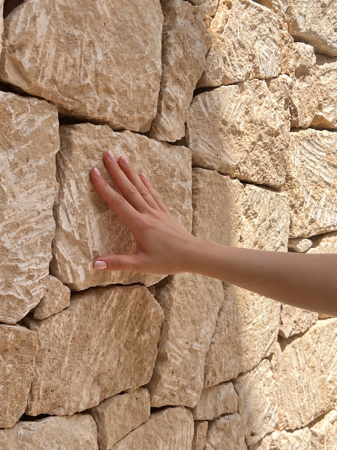 A person's hand touching a beige limestone stone wall.