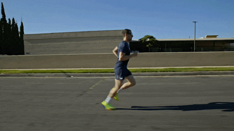 A person dressed in blue running on a paved road during daytime with a modern building and trees in the background.