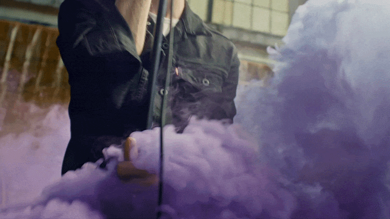 Person wearing a black jacket using a device that emits purple smoke.