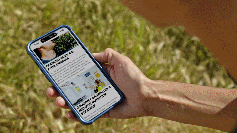 A person holding a smartphone outdoors displaying a website or news article about training and nutrition.