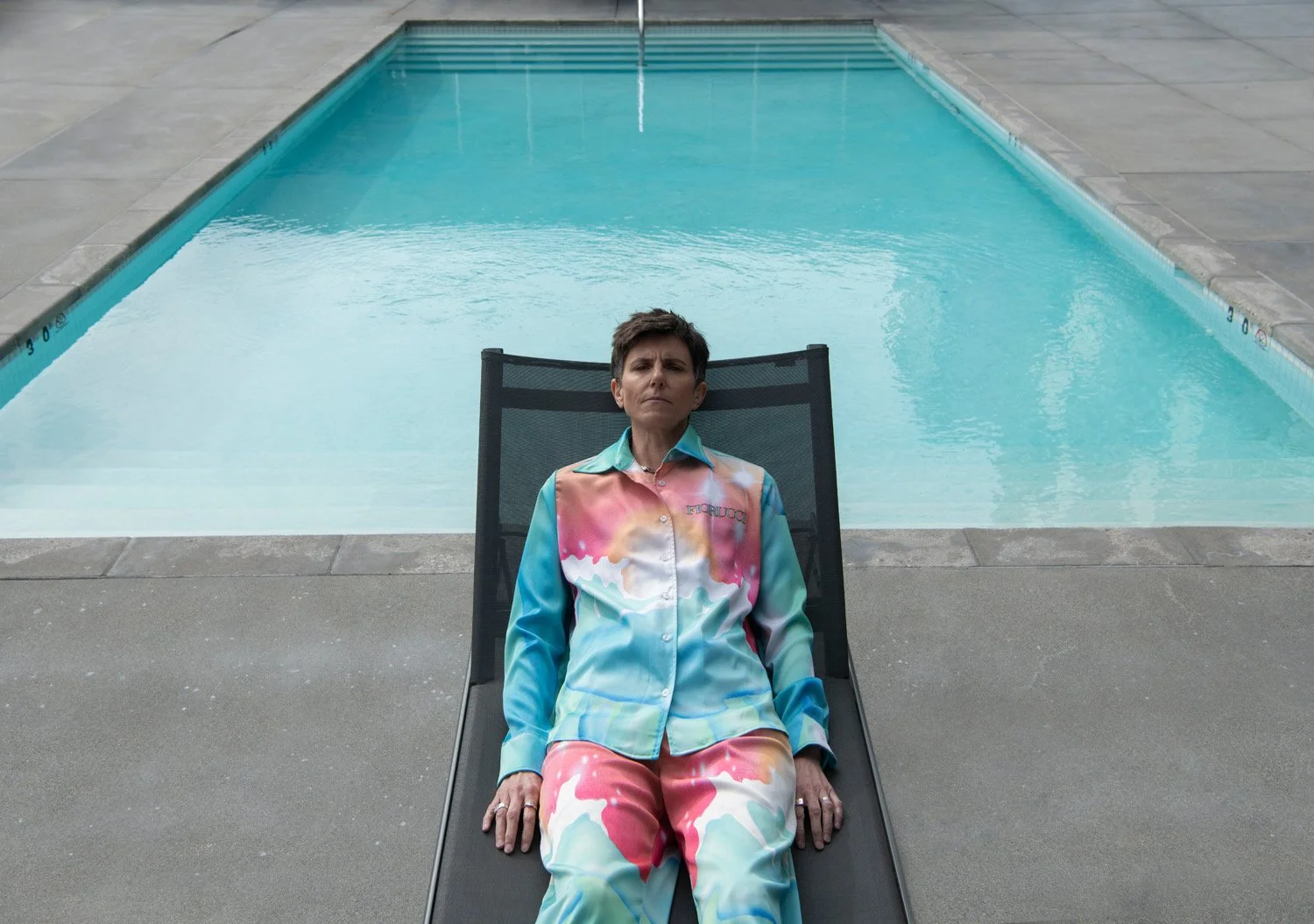 A woman wearing colorful pajamas sitting on a lounge chair next to a swimming pool.