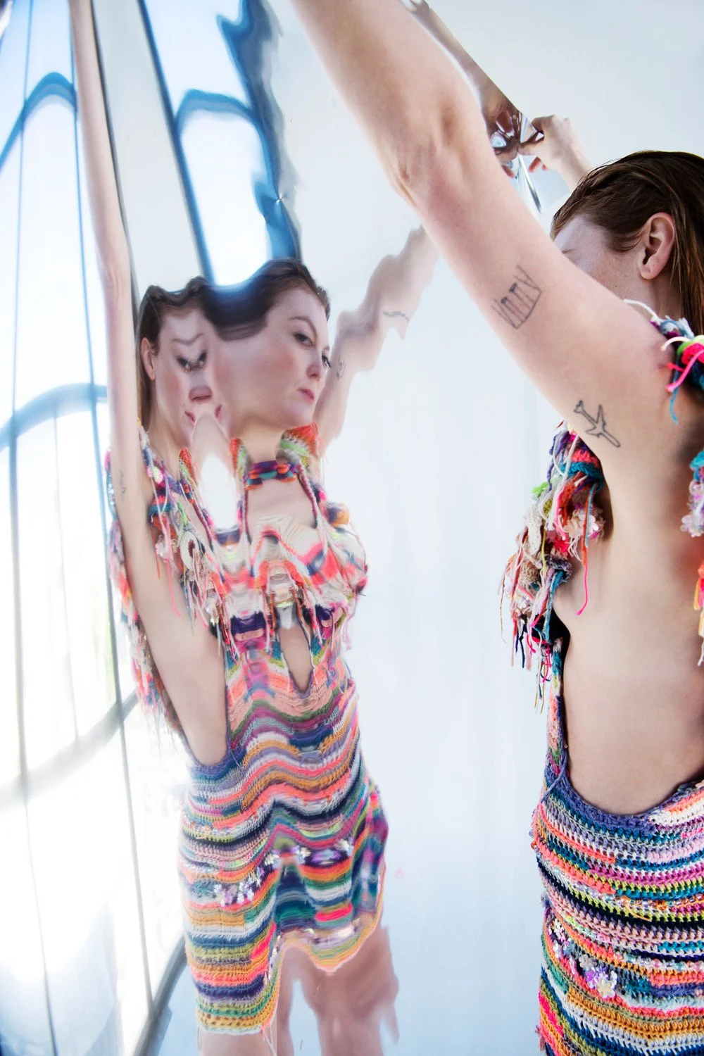 Two women in colorful, crocheted outfits taking a selfie in front of a mirror that distorts their reflection.