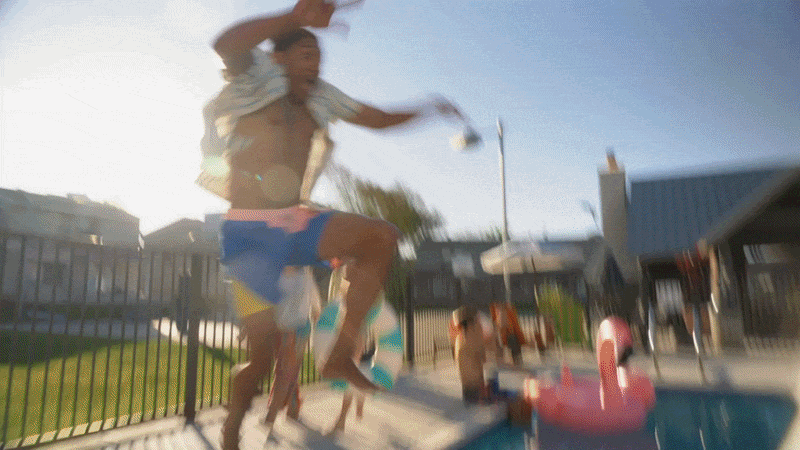 Person jumping into a swimming pool on a sunny day with a city skyline in the background.