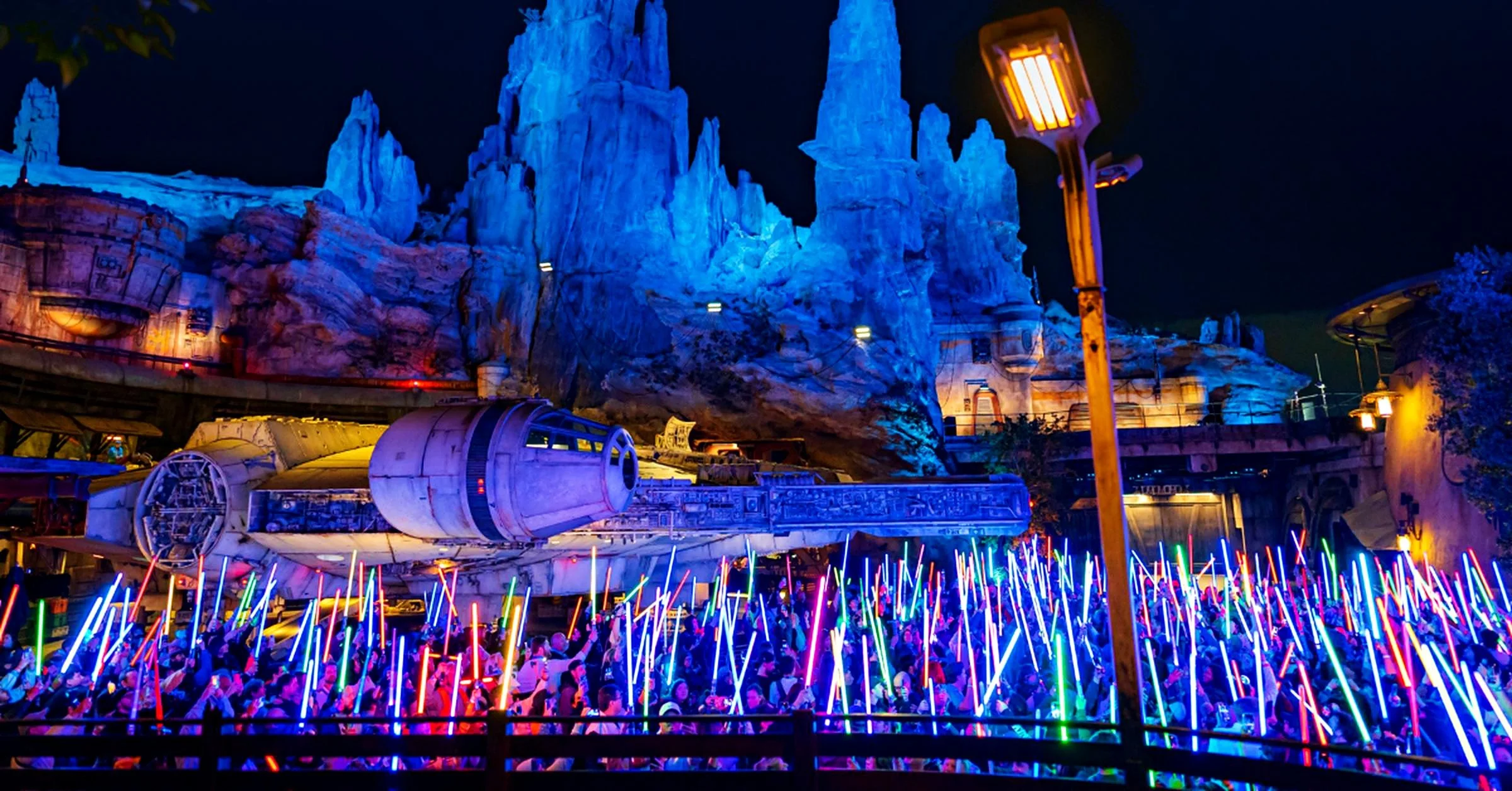Millennium Falcon in Star Wars: Galaxy's Edge at night with guests raising glowing lightsabers