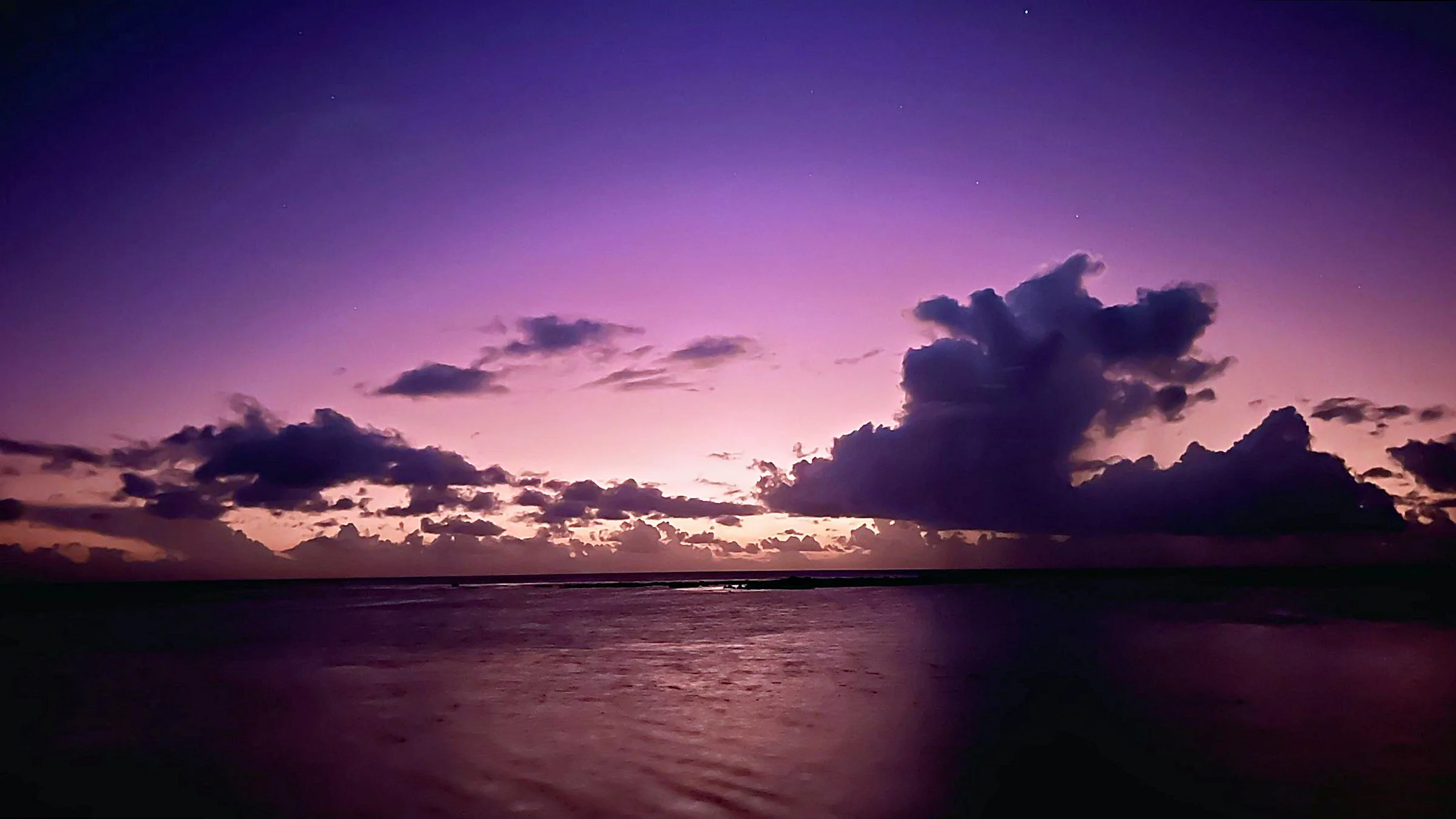 Remote ocean horizon at twilight under a violet sky and towering clouds