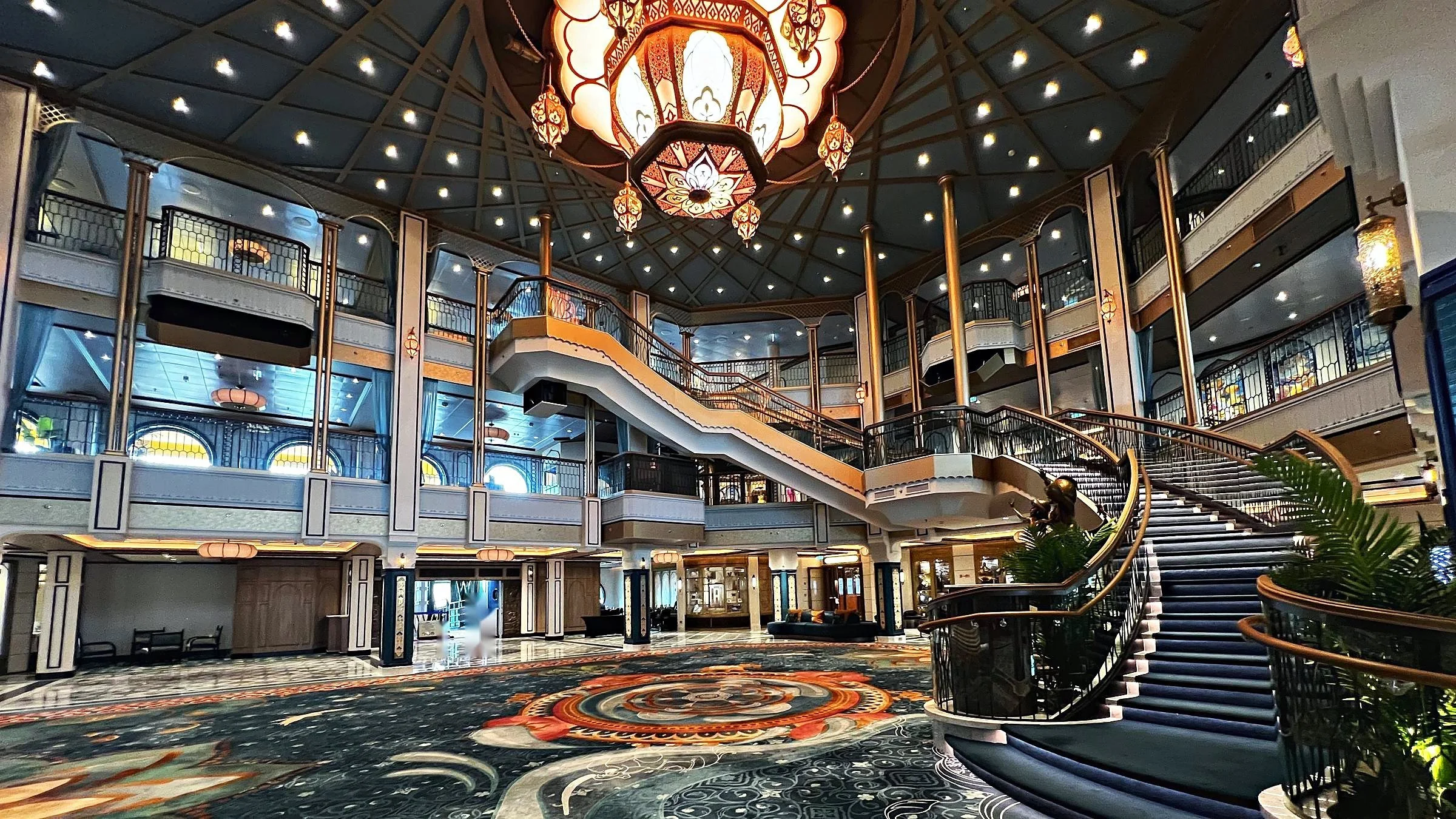Grand atrium of a Disney Cruise Line ship with an ornate lantern chandelier and sweeping staircase