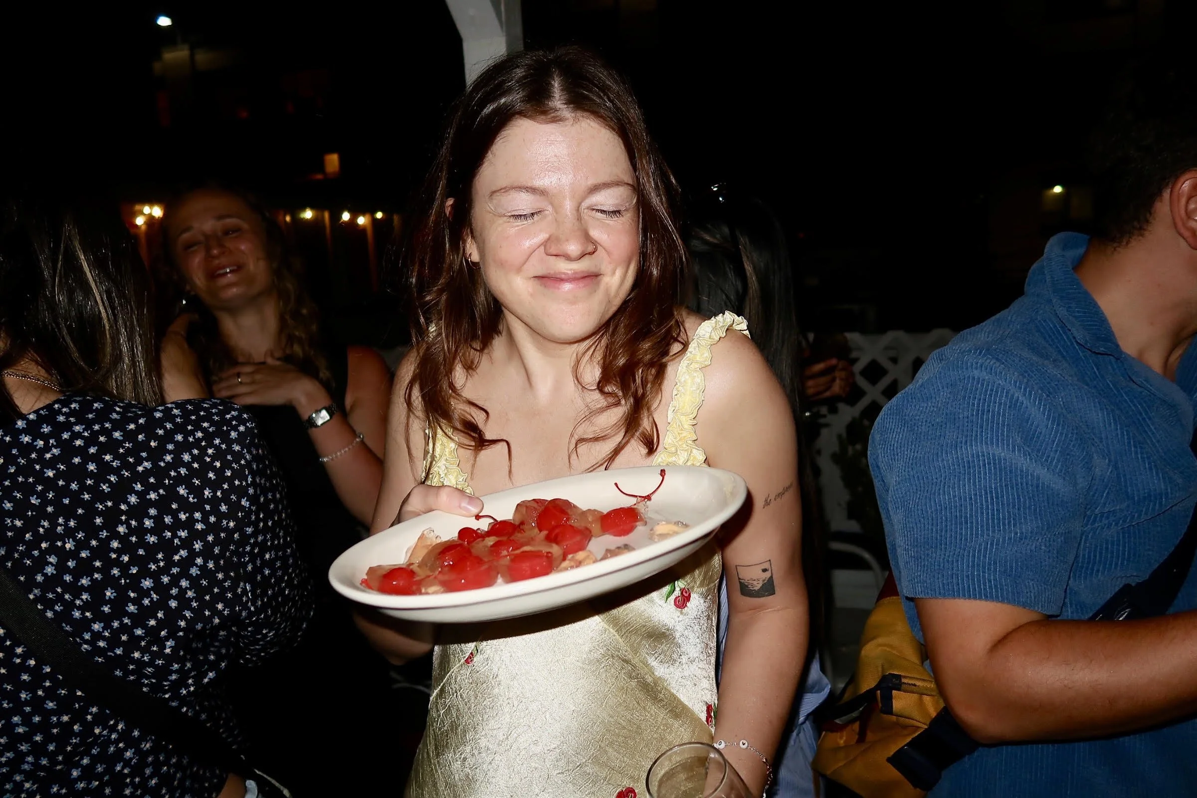 A woman with red hair and a yellow dress holding a plate of cherries and strawberries at a celebration or party.