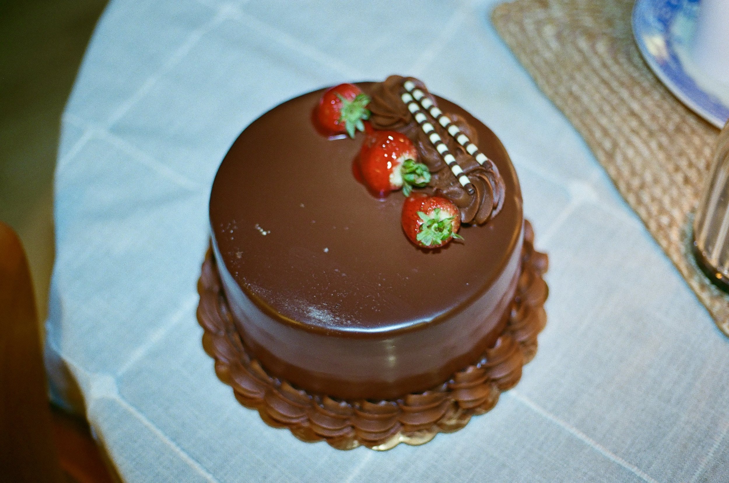 Chocolate cake topped with strawberries and white chocolate striped decorations on a woven placemat.