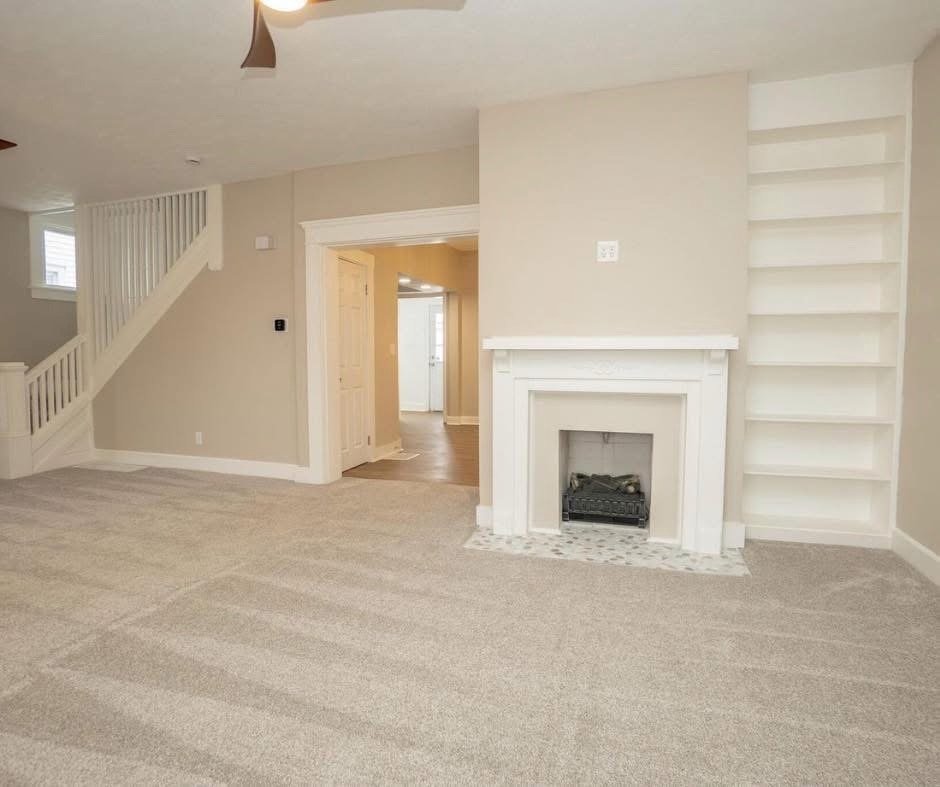 Living room with beige walls, carpet flooring, a white fireplace, and built-in shelves to the right of the fireplace.
