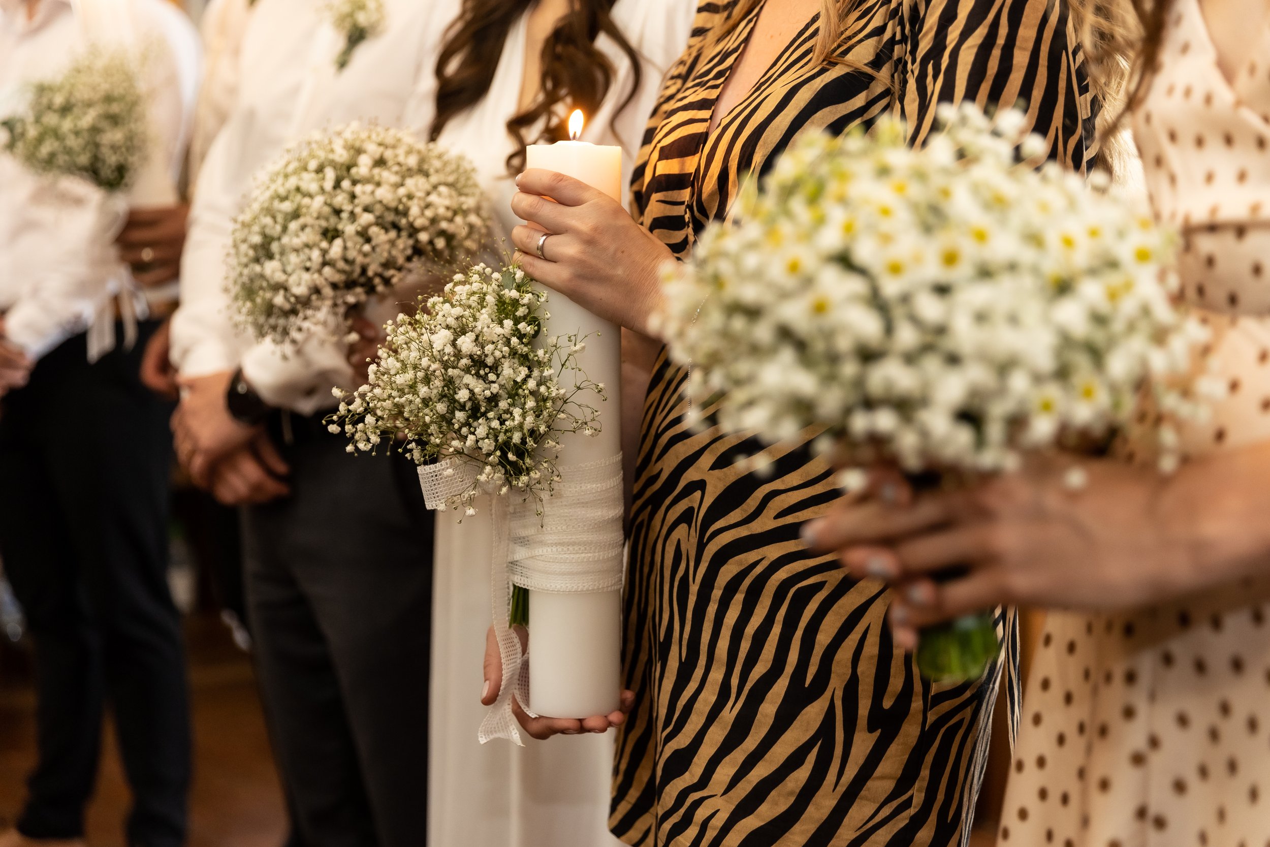 Women holding bouquets of white flowers and a candle during a ceremony.