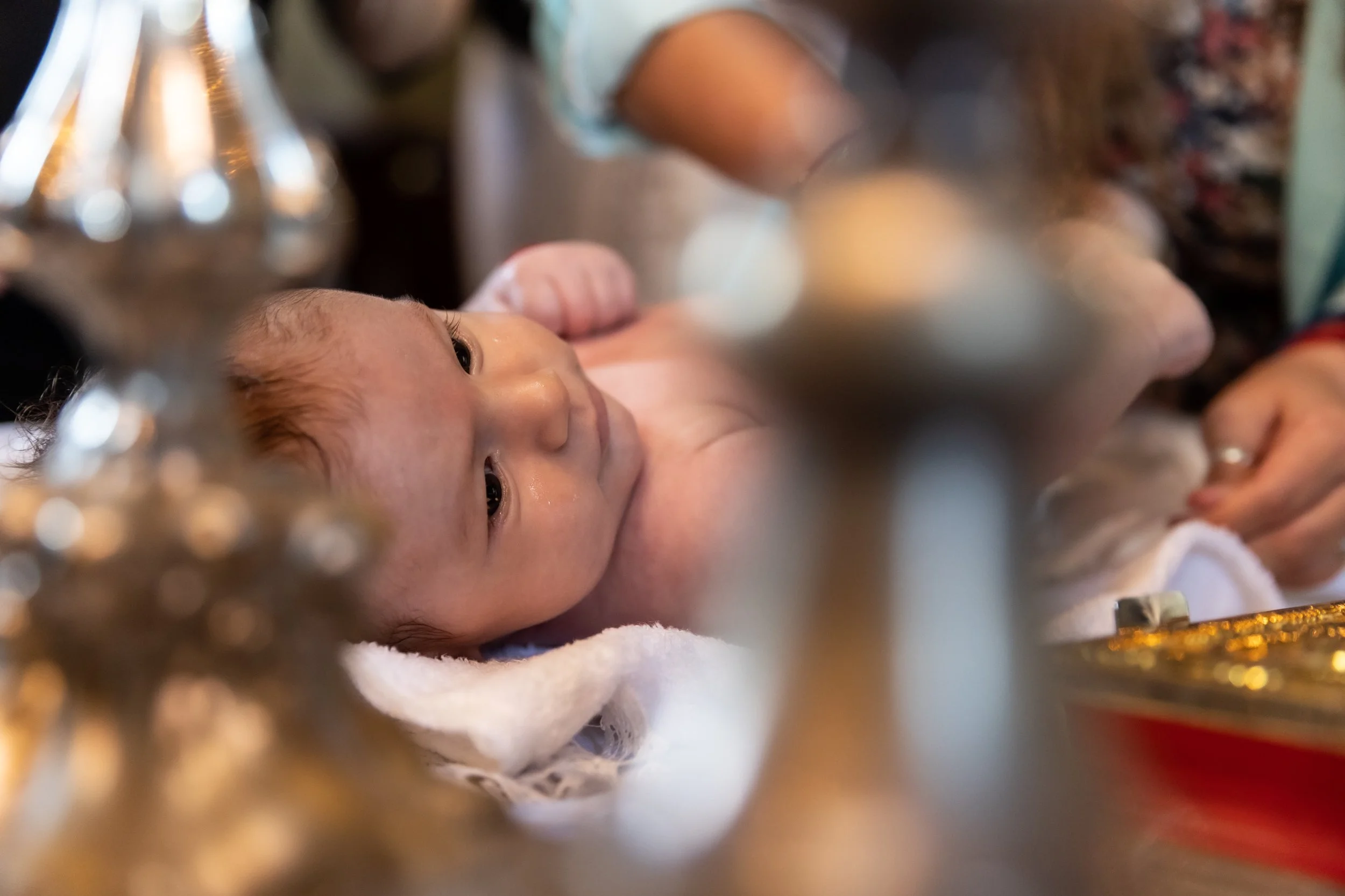 A baby lying on a bed with a blanket, viewed through a glass or decorative frame, with a blurred background.