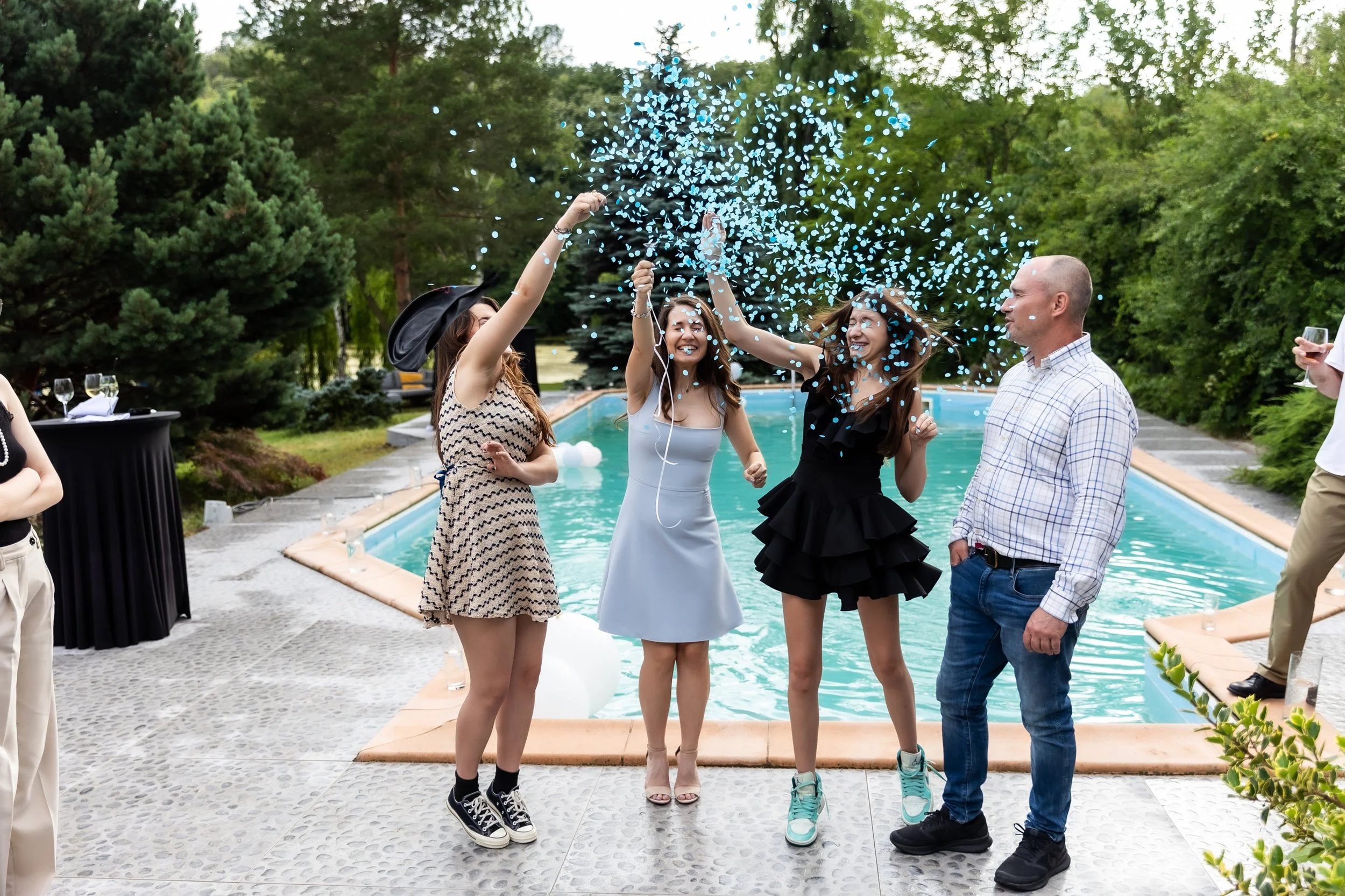 Group of people celebrating by a pool with floating blue confetti and champagne glasses.