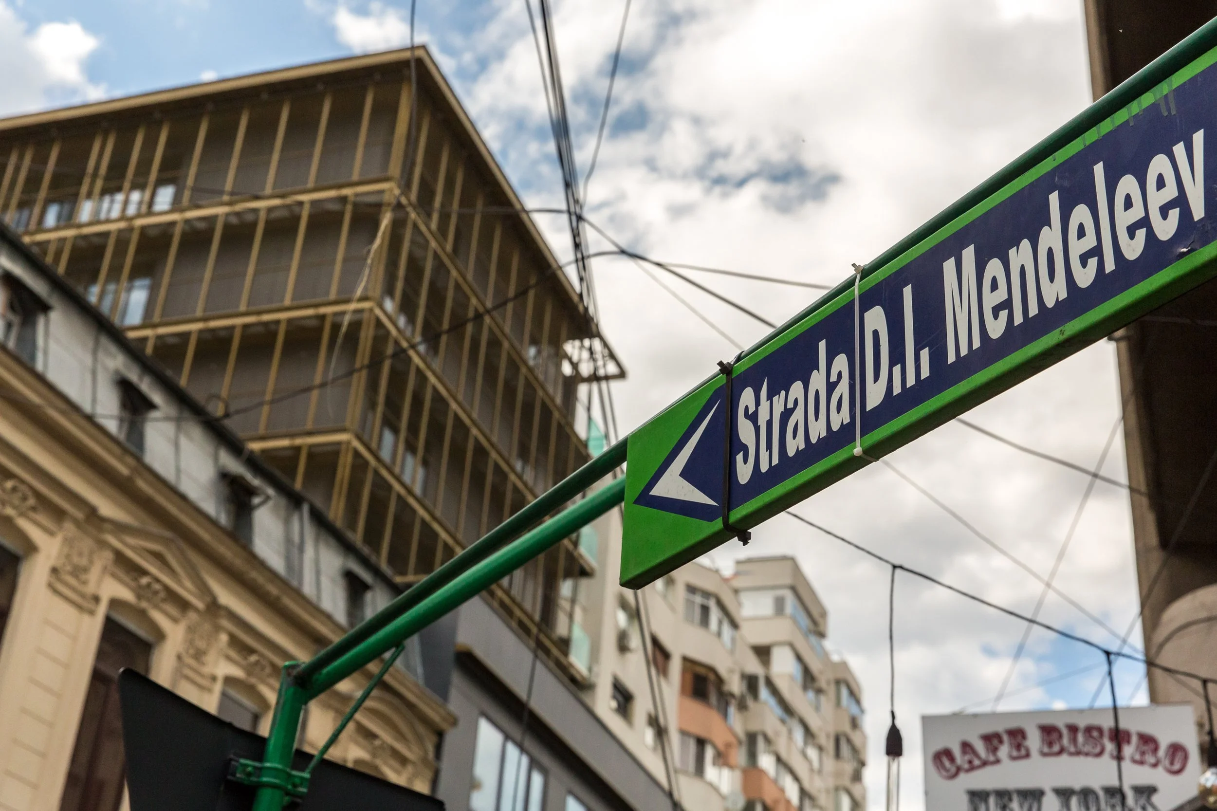 Street sign pointing to Stadion A. Le Coq Mendeleyev and a multi-story building under construction with unfinished balconies visible.