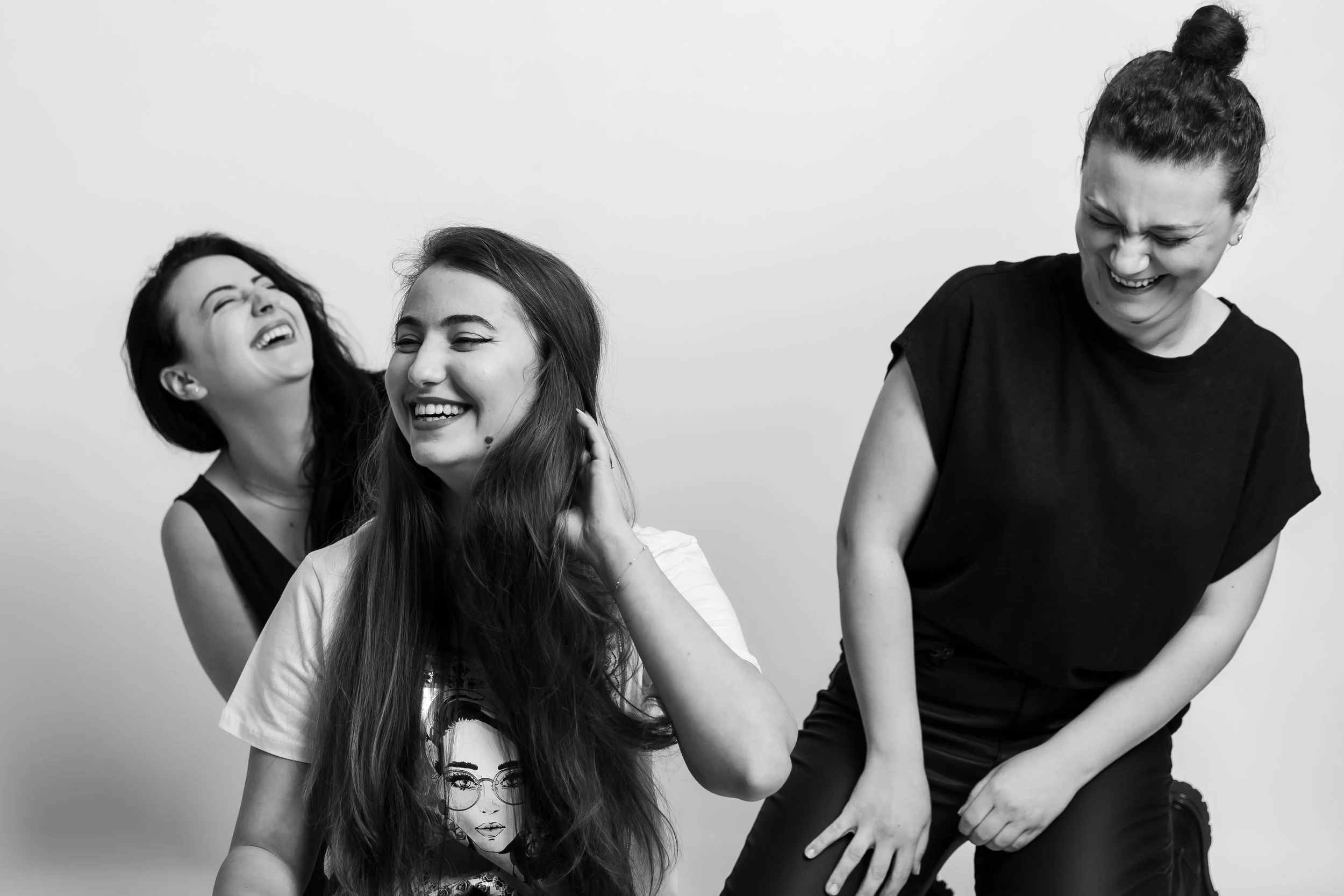 Four women laughing and smiling, two on the left and two on the right, against a plain background.