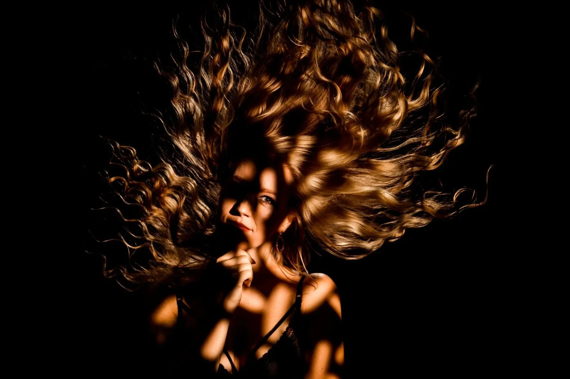 A woman with curly blonde hair spread out around her head, partially covering her face against a dark background.
