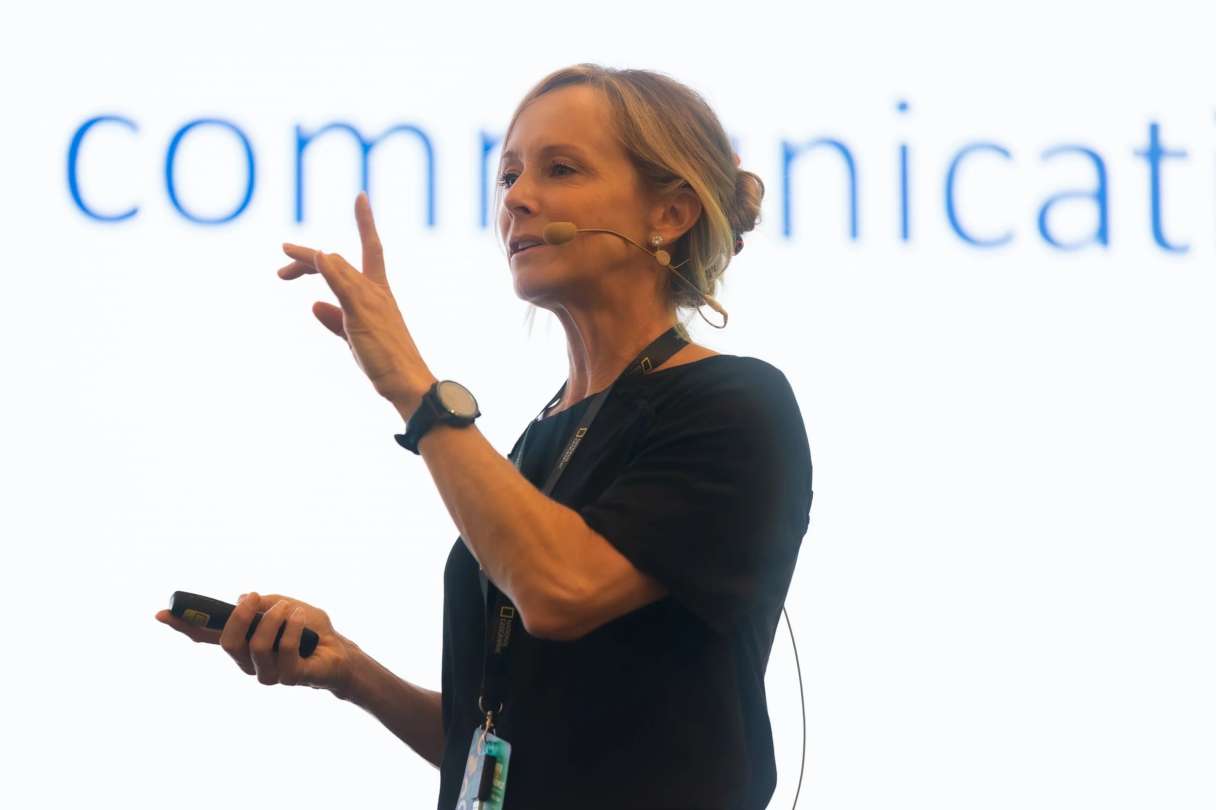 A woman with a headset giving a presentation in front of a screen with the word 'communication' displayed.