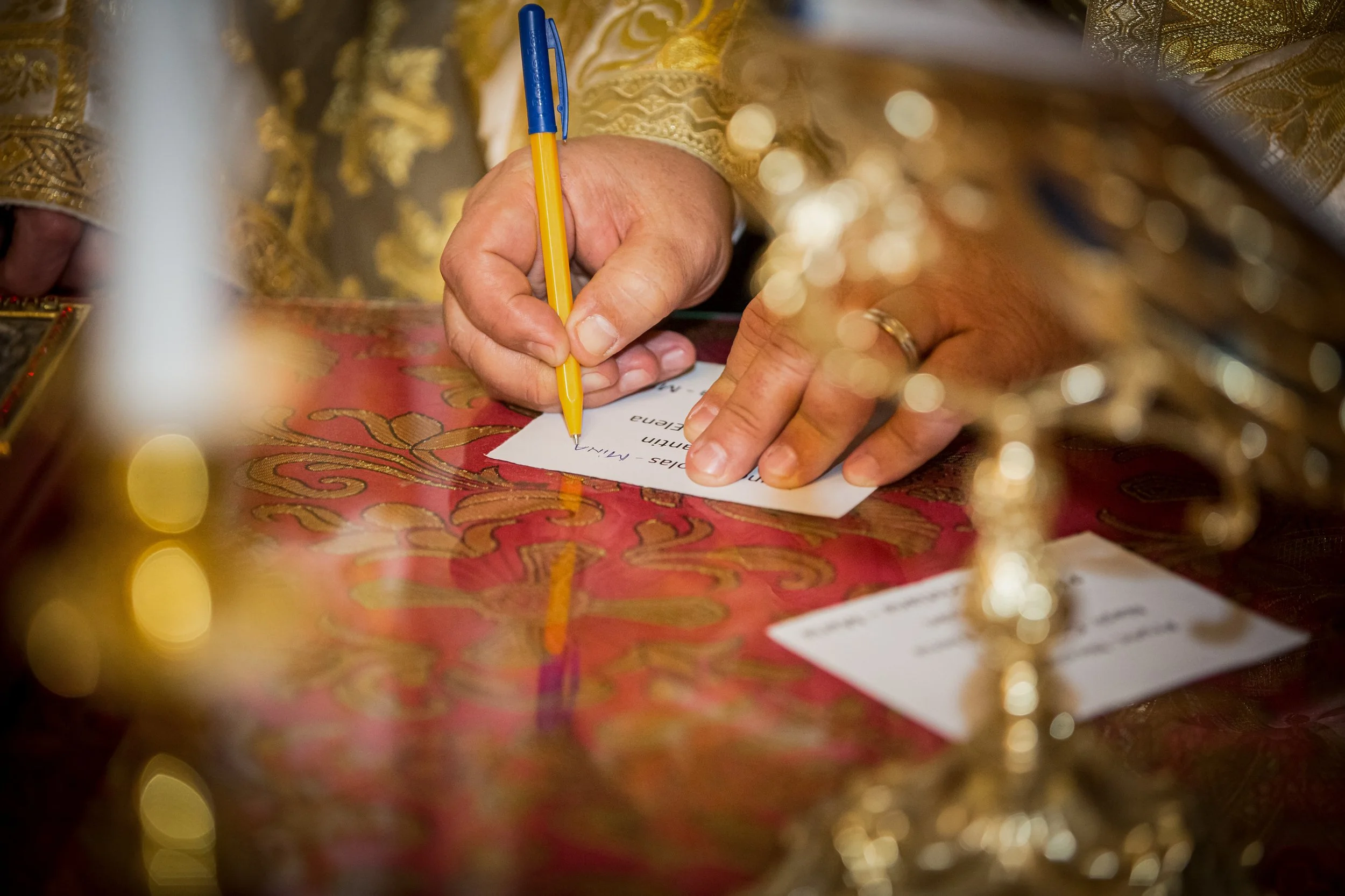 A person's hand writing on a piece of paper with a yellow pen, surrounded by ornate gold and red fabric.