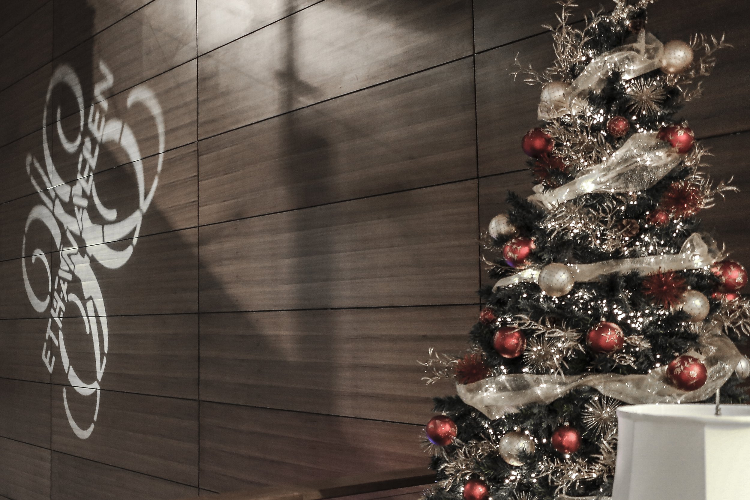 Decorative Christmas tree with red, white, and gold ornaments and ribbons, placed against a wooden wall background.