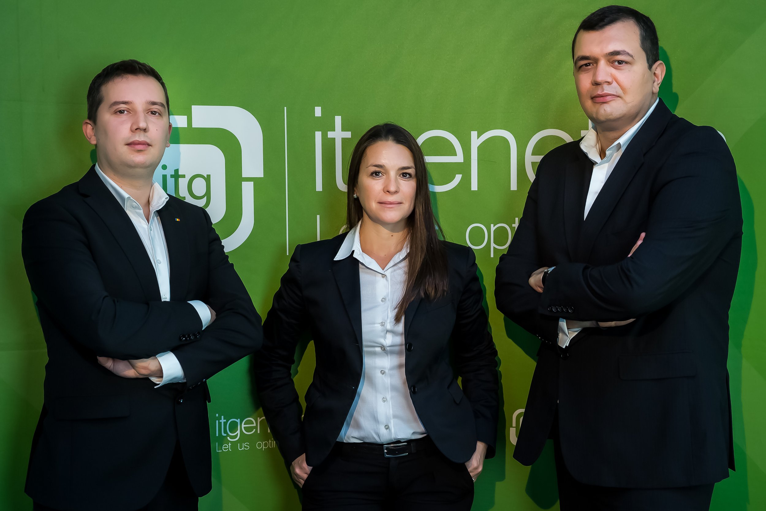 Three professionally dressed individuals, two men and one woman, standing in front of a green background with white text and logo. The group appears confident with arms crossed and serious expressions.