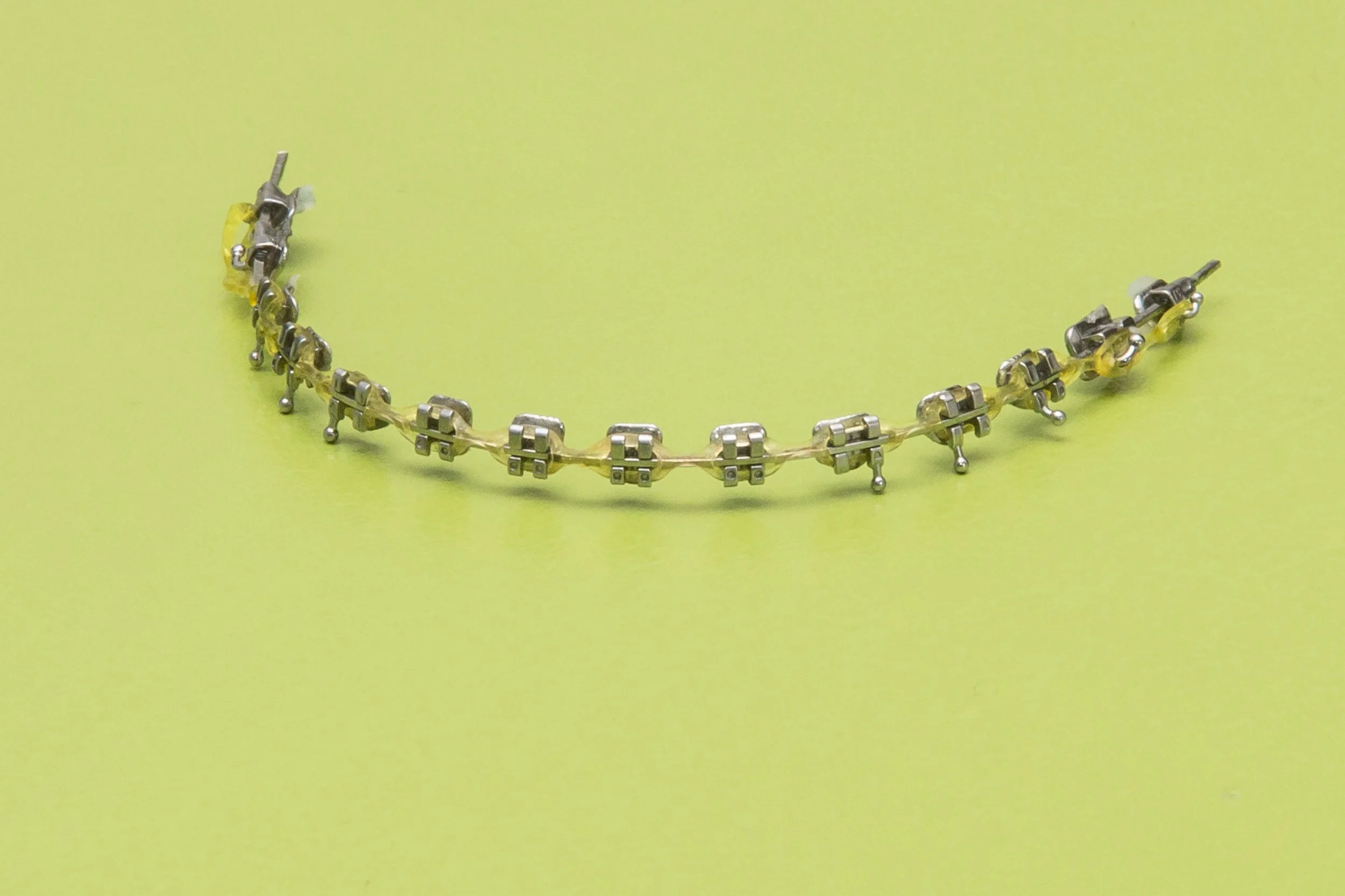 A yellow bracelet made of metal and plastic links on a yellow background.