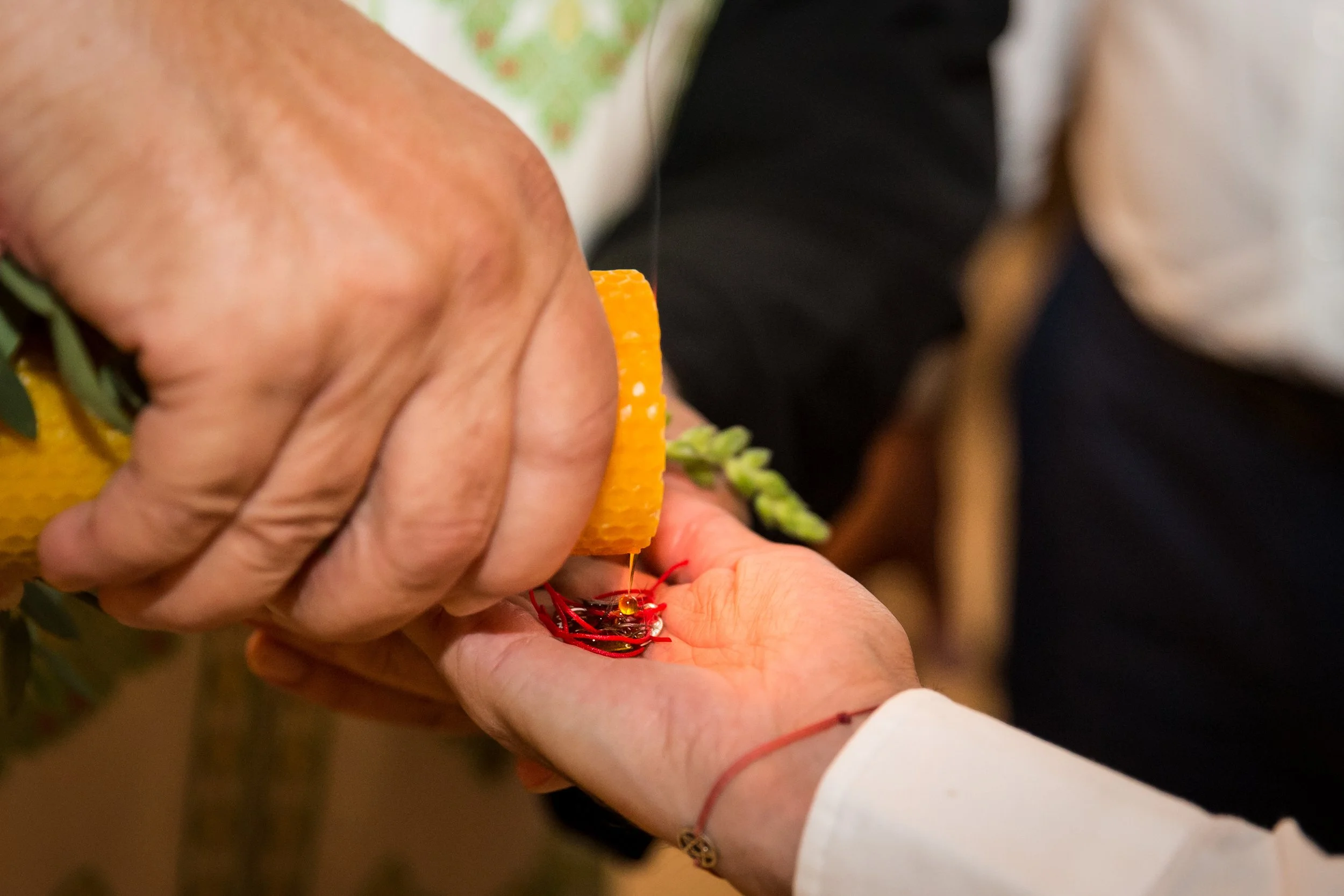 Close-up of hands performing a traditional craft or ceremony involving sewing or embroidery, with visible sewing tools and thread.