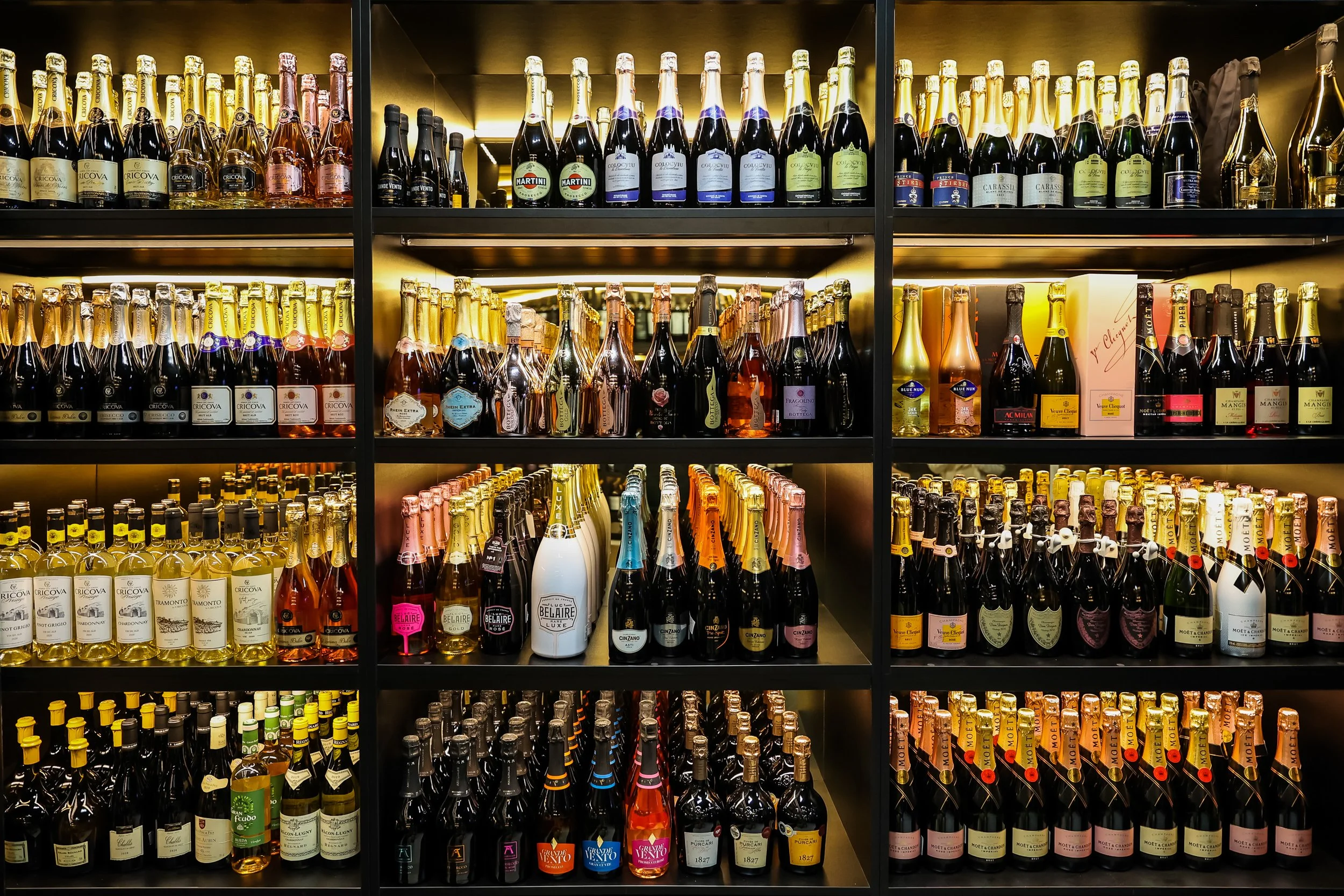 Shelf of various bottles of sparkling wine and champagne in a store display, organized by brand and type.