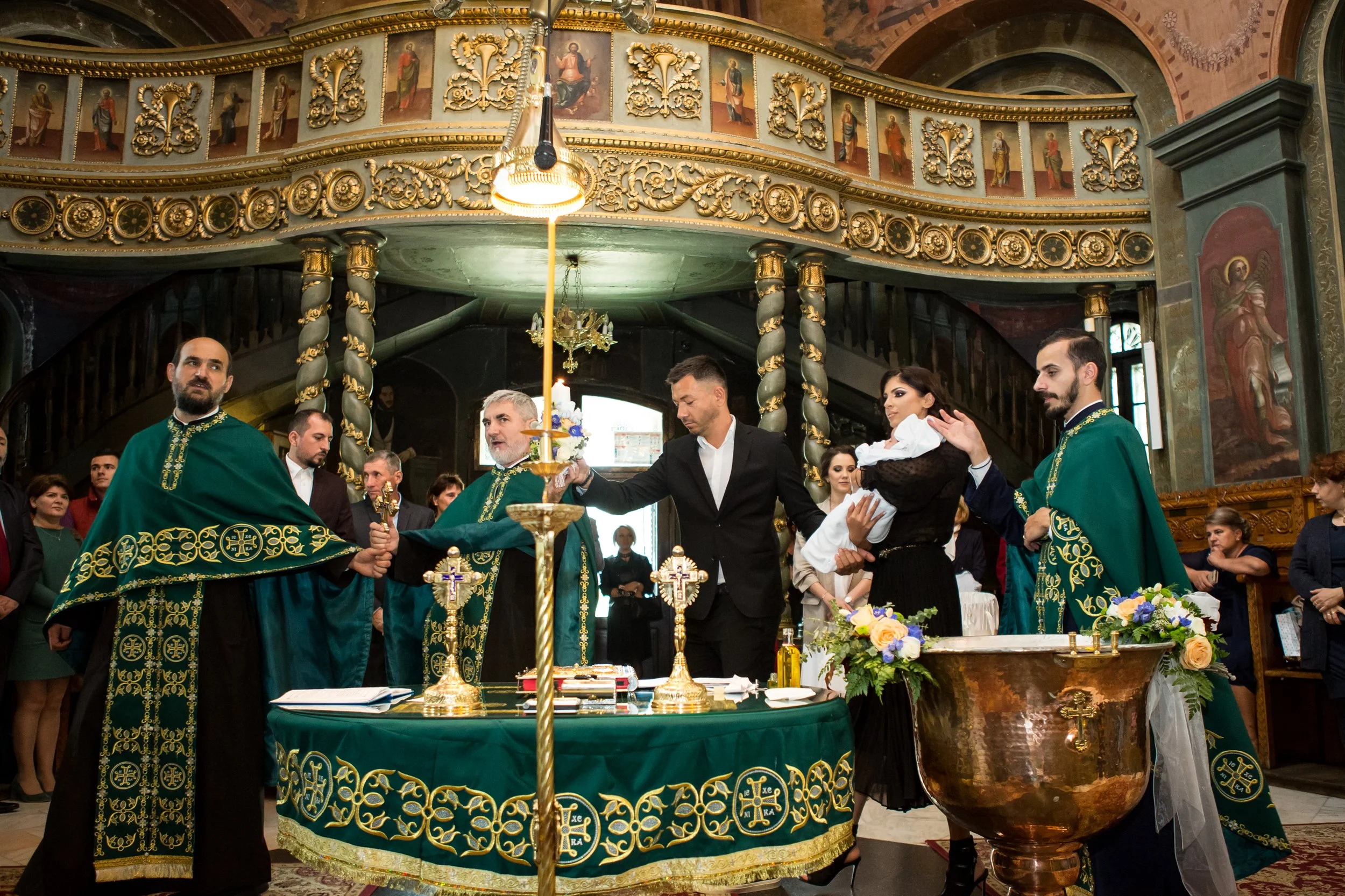 A religious ceremony inside a church with priests dressed in green robes near an altar, surrounded by congregation members, ornate decor, and religious icons.
