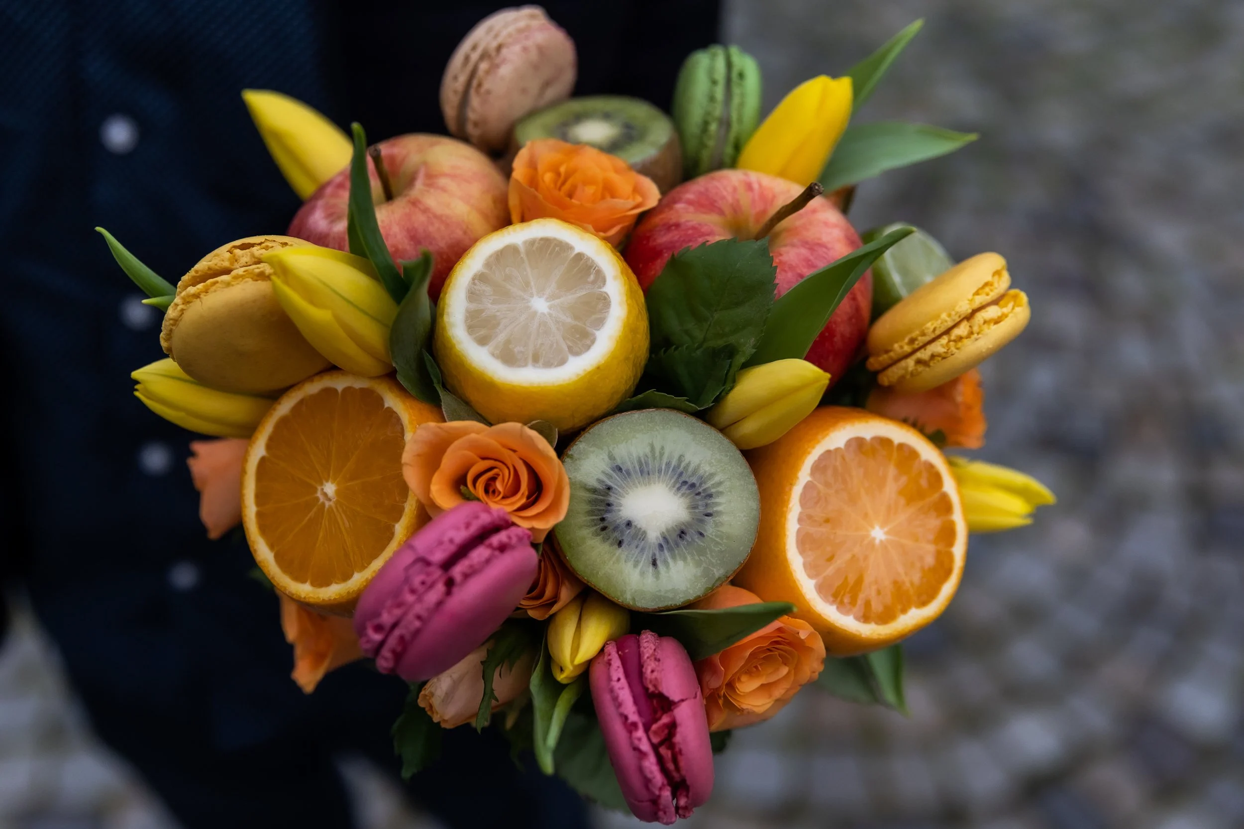 A bouquet of flowers, fruits, and macarons, including lemon slices, strawberries, kiwis, and peach roses.