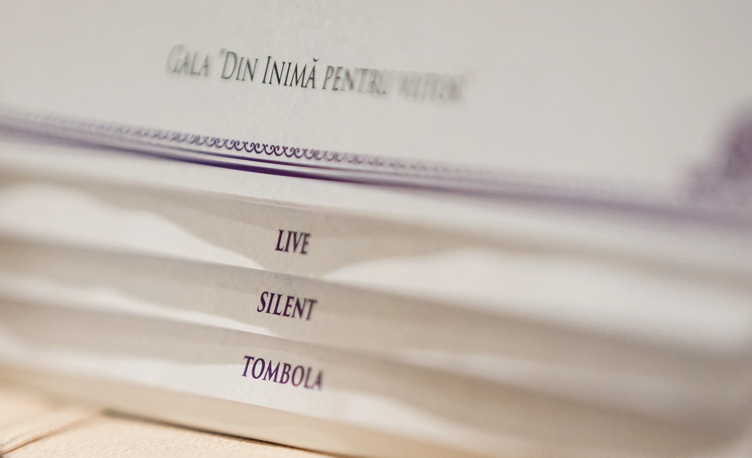 Close-up of a paper or booklet with typed text, showing the words 'LIVE', 'SILENT', and 'TOMBOLA' in purple ink.
