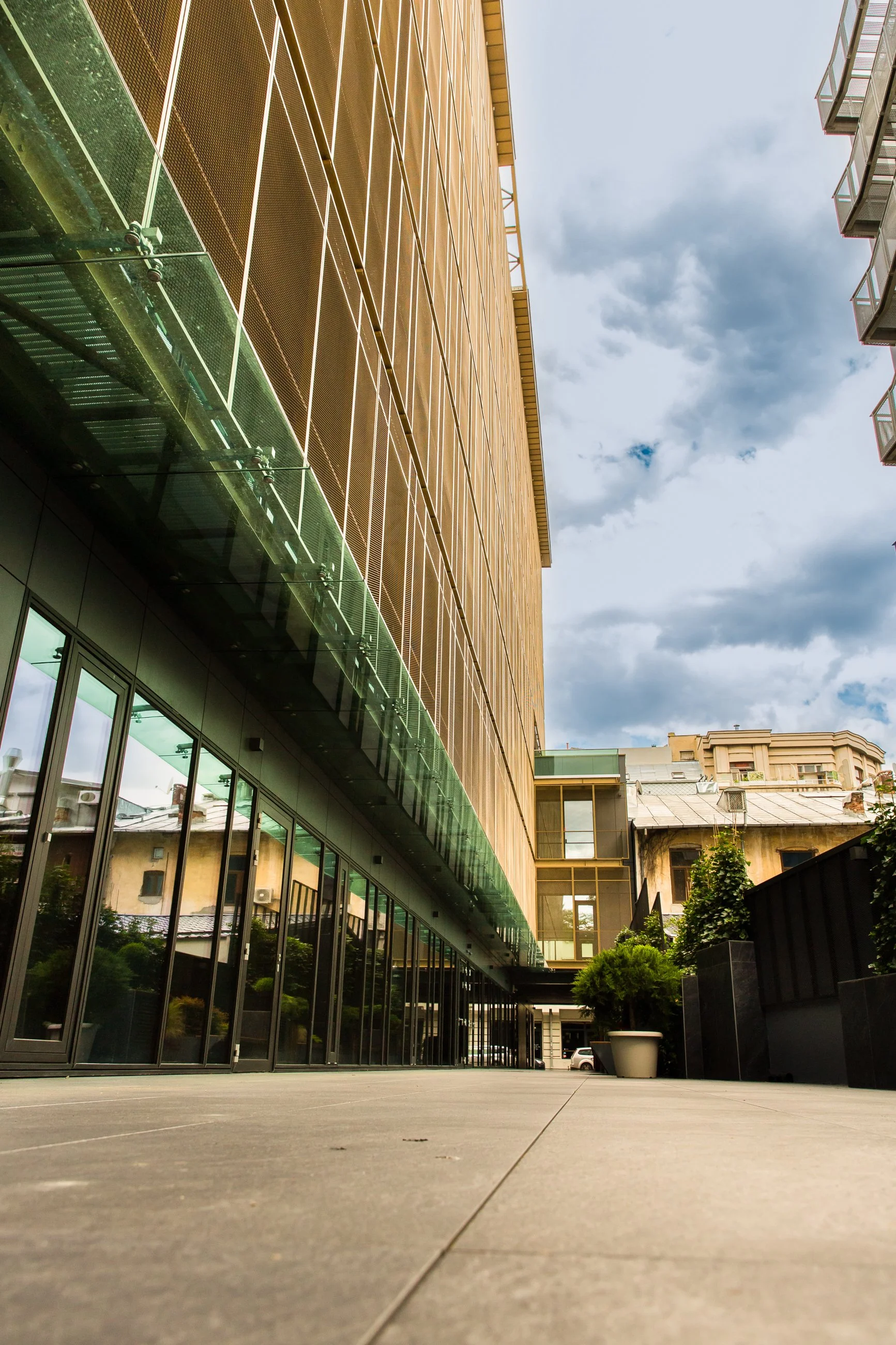 A modern building with glass windows and a wooden upper facade, seen from a low angle during daytime with cloudy sky.