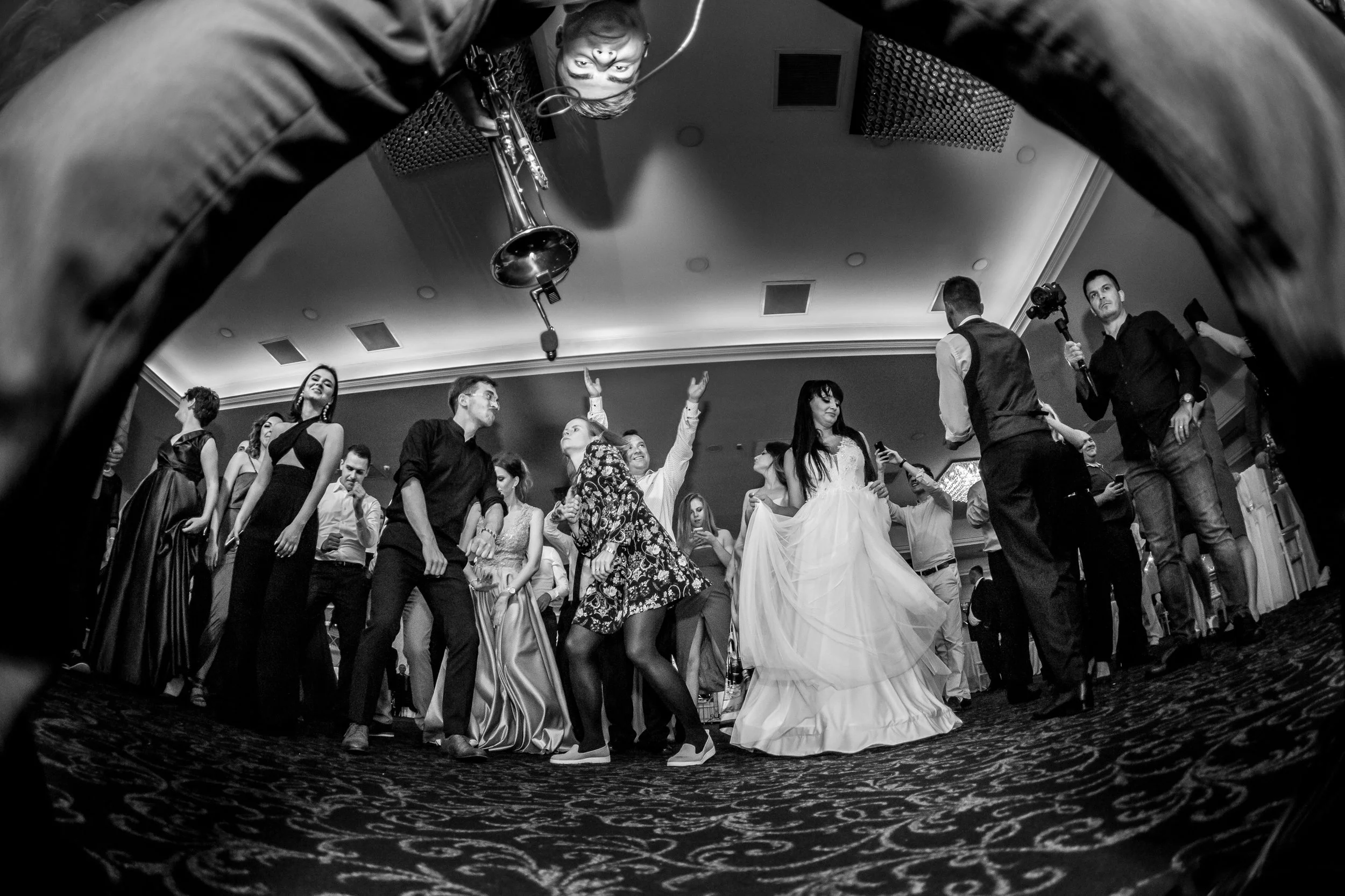 People dancing at a celebration, viewed from a low angle with a decorative patterned carpet in the foreground.
