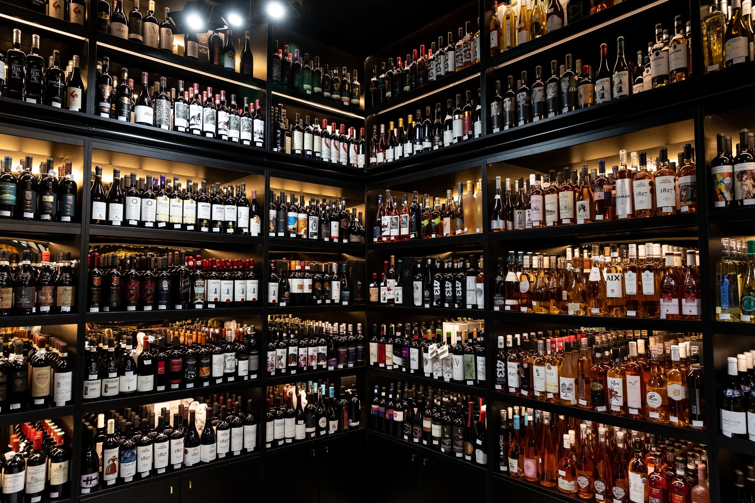 A large wine store with multiple shelves filled with wine bottles, arranged by type and brand, under warm lighting.