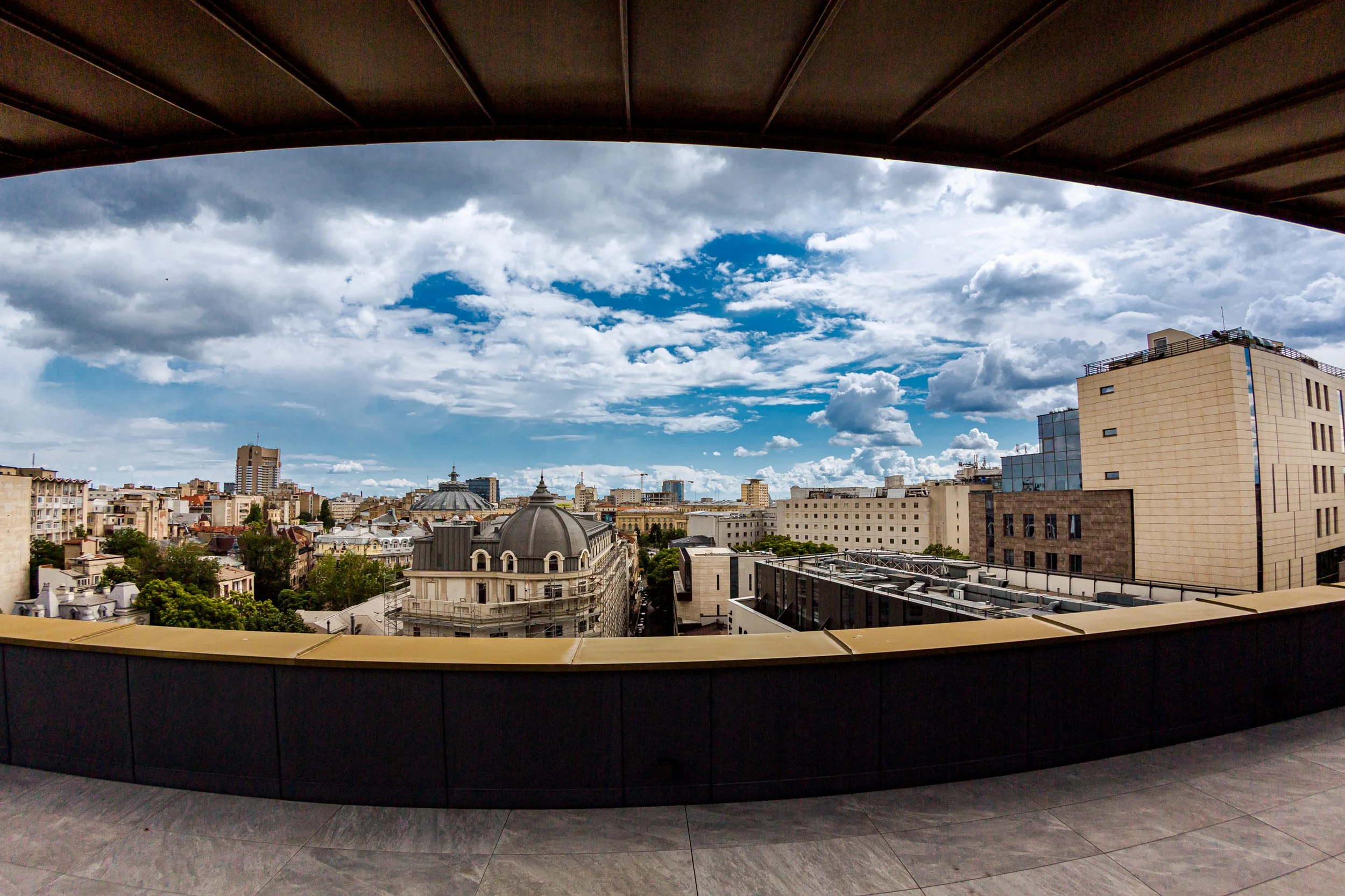 City skyline view seen from a balcony with a curved black railing, under a partly cloudy sky.