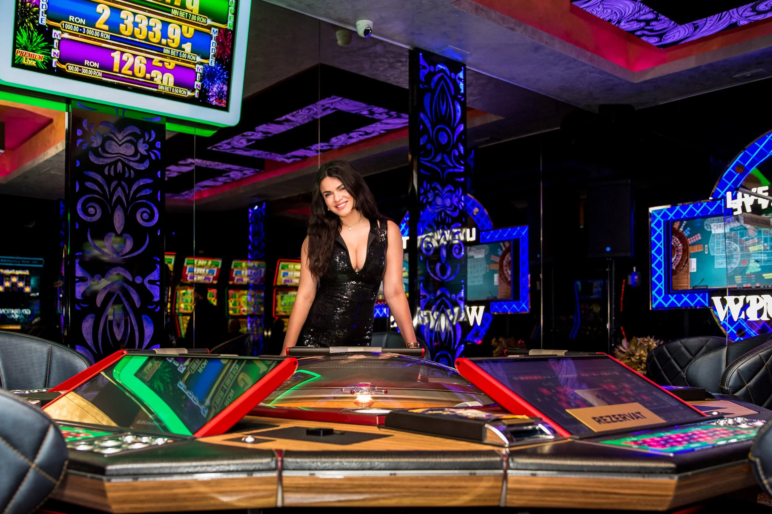 A woman in a black dress is playing gambling at an casino, surrounded by slot machines, electronic screens, and decorative mirrors with purple lighting.