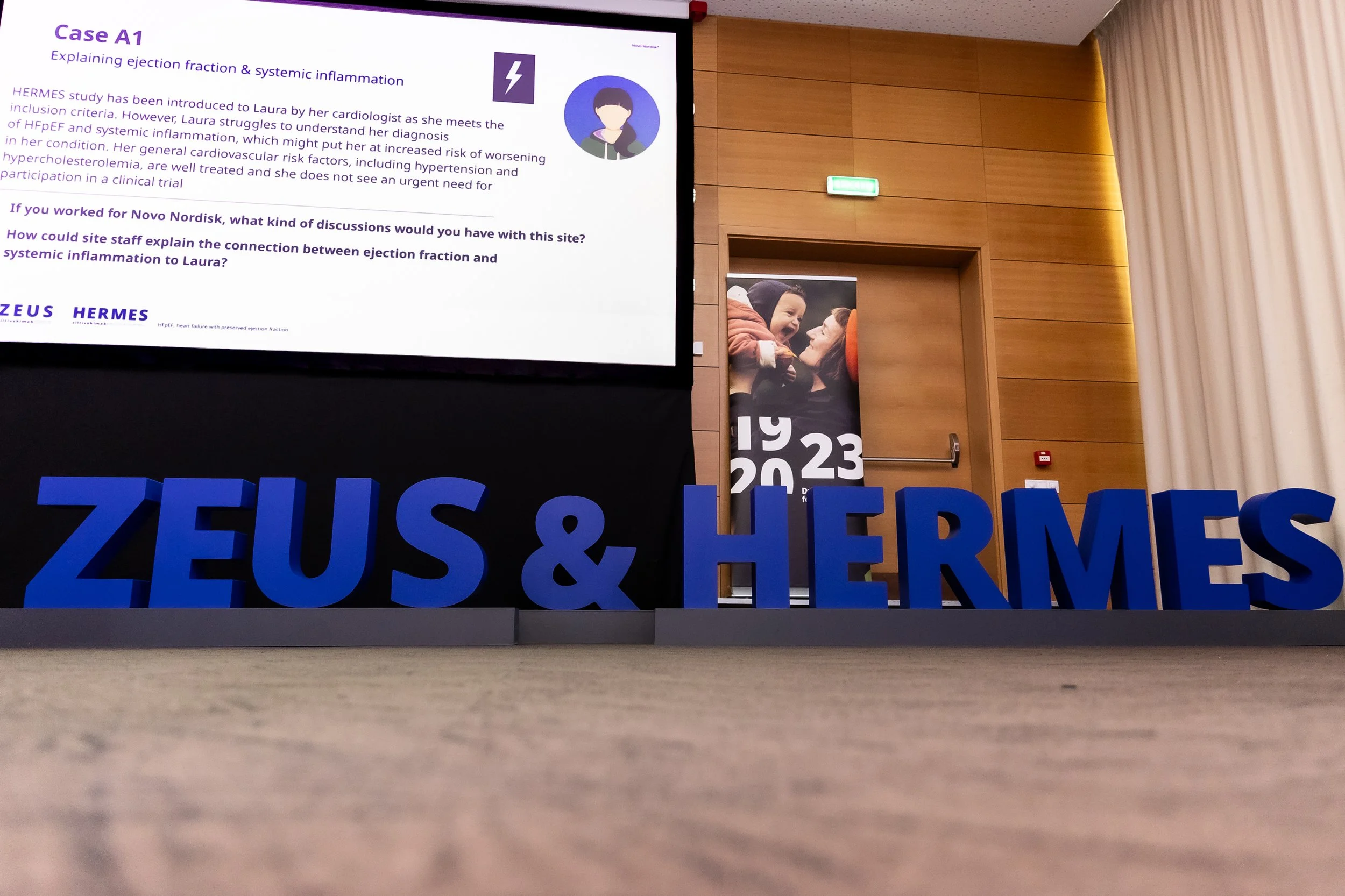 Photograph of a presentation slide about a medical case, titled 'Case A1,' with the subtitle 'Explaining ejection fraction & systemic inflammation.' The slide features a digital illustration of a person with dark hair and a purple background, a purpl
