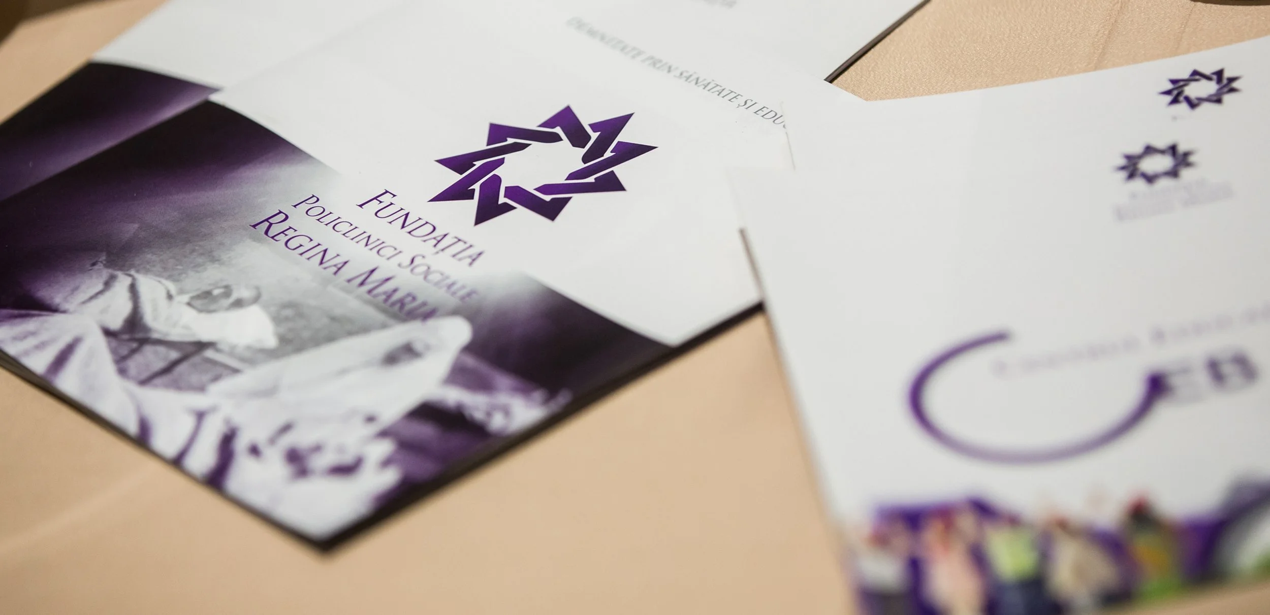Close-up of printed materials with a purple geometric logo, including a brochure and a flyer, placed on a beige surface.