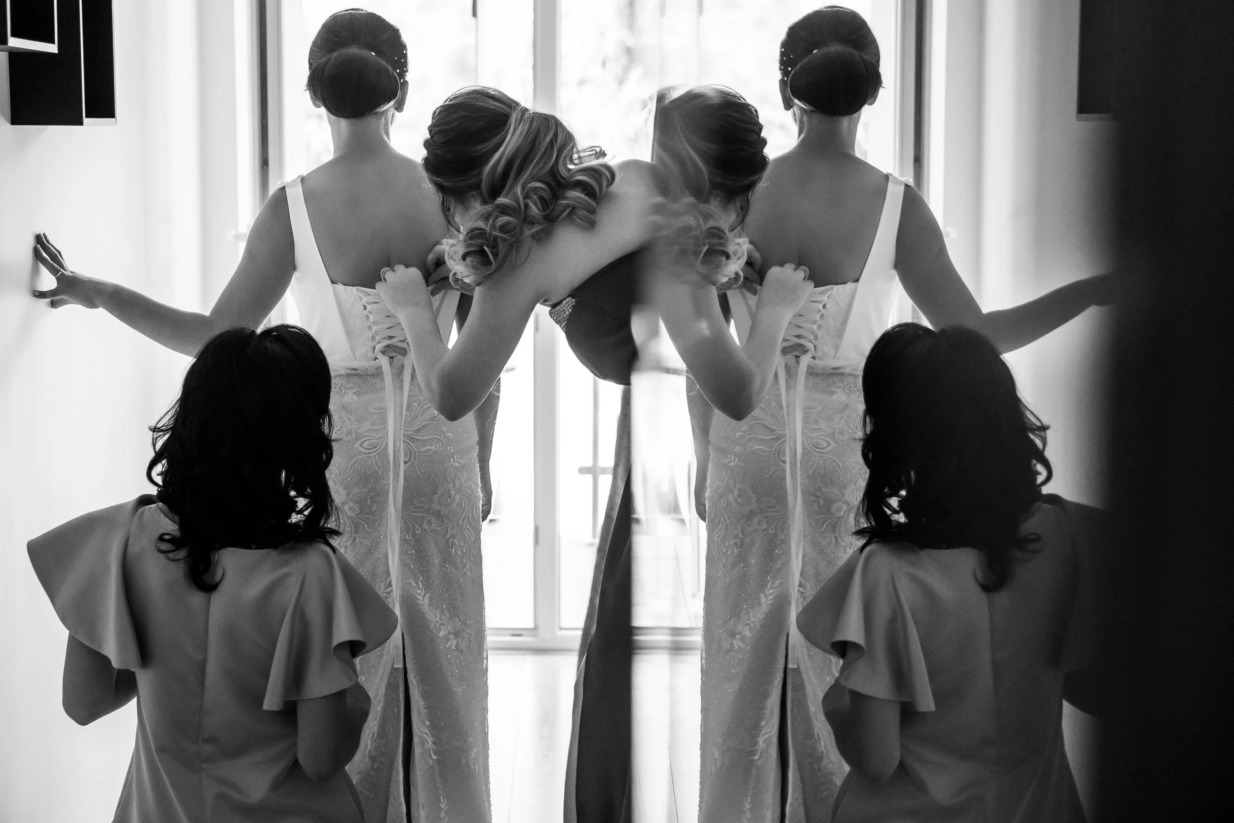 Black and white photo of three women in elegant dresses, surrounded by reflections of themselves in a mirror, in a mirror effect.