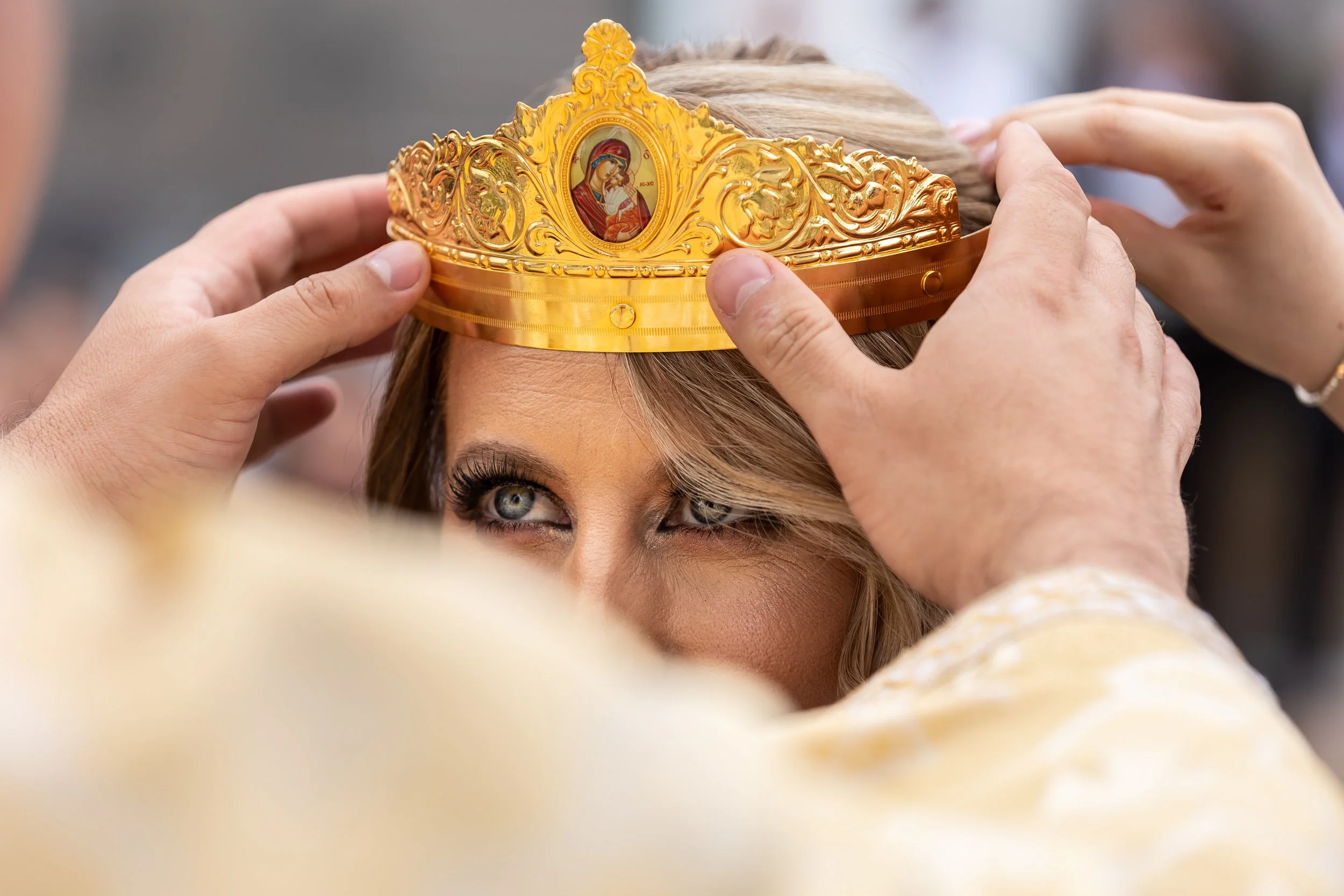Person placing a golden crown with religious iconography on a woman's head during a ceremony.