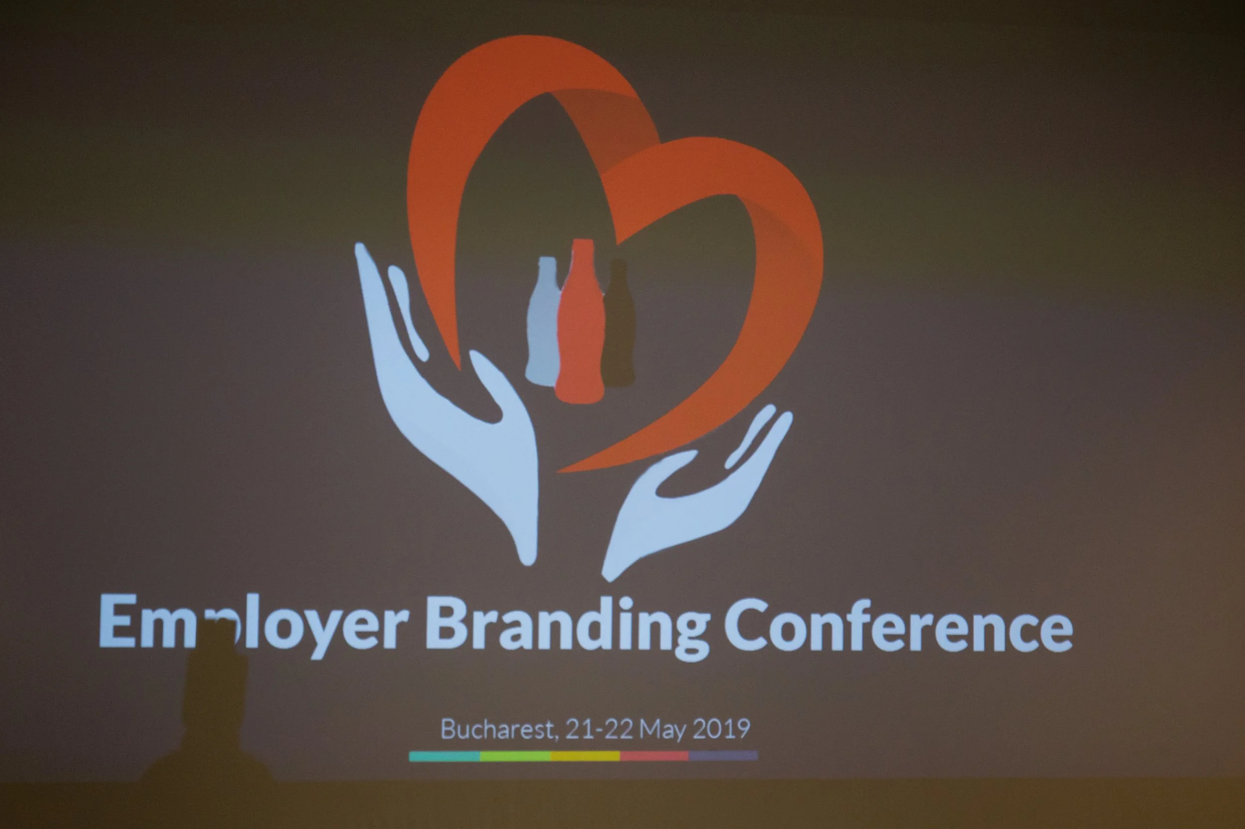 Logo with orange heart and white hands holding it, text reads 'Em•ploy•er Branding Conference', held in Bucharest on May 21-22, 2019.