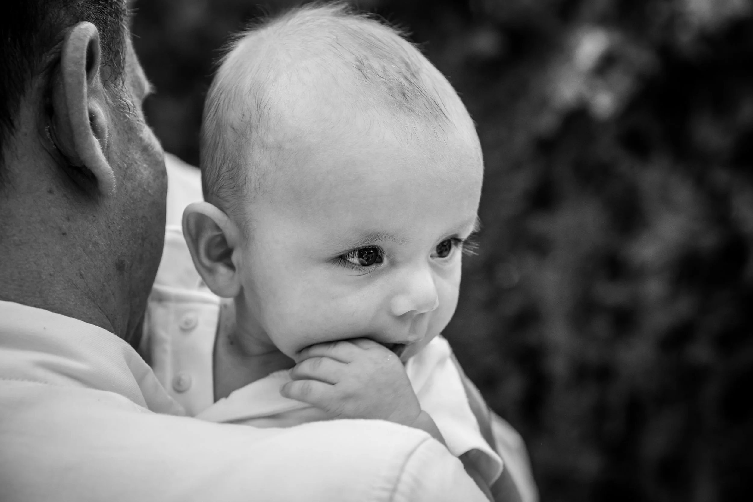 Close-up of a man holding a young child, both looking intently into the distance. Black and white photo,Outdoor setting.