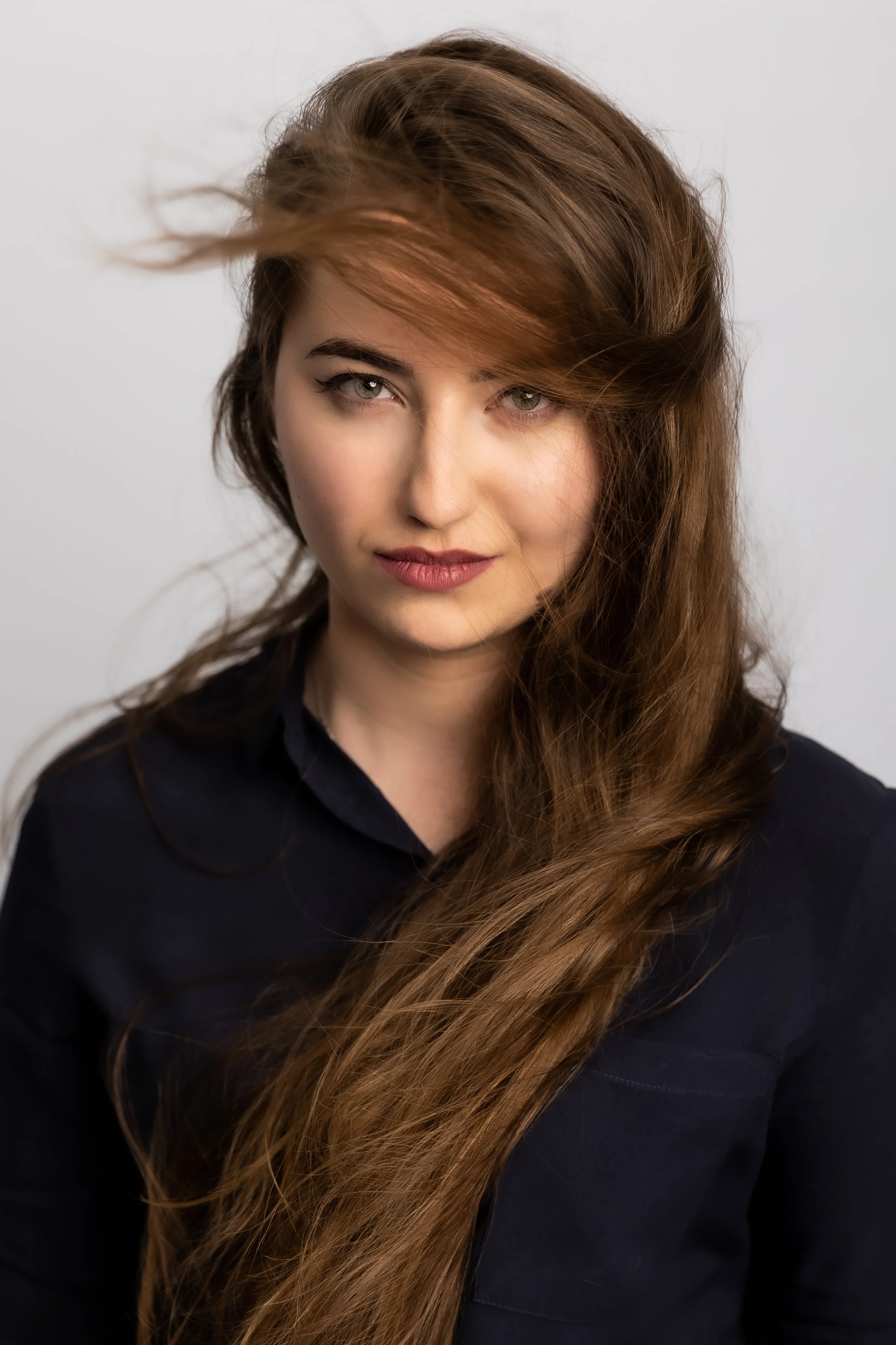 A woman with long, wavy auburn hair, green eyes, and light makeup wearing a black shirt against a white background.