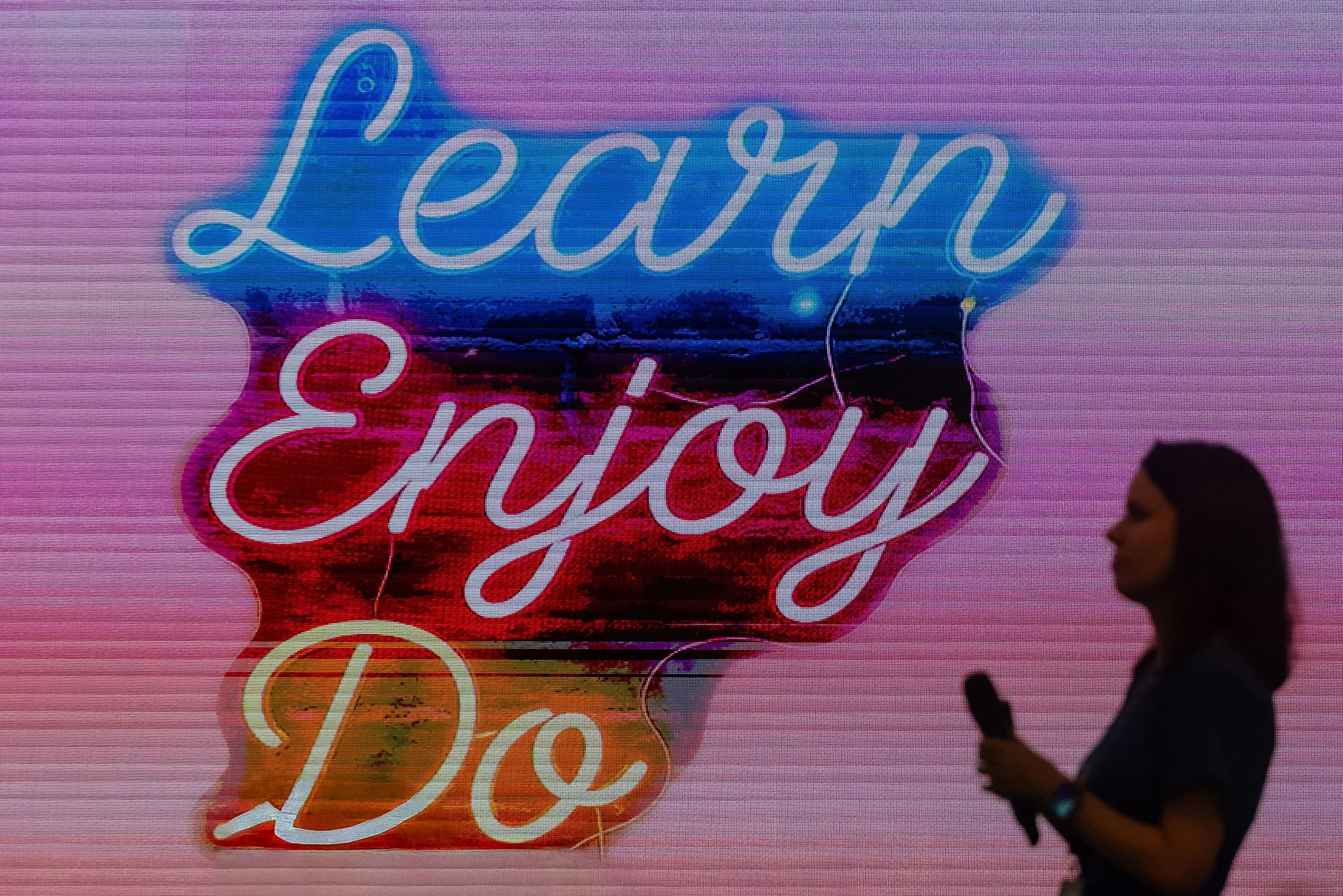 Illuminated neon sign reading 'Learn and Enjoy' against a colorful background, with a person walking past in silhouette.