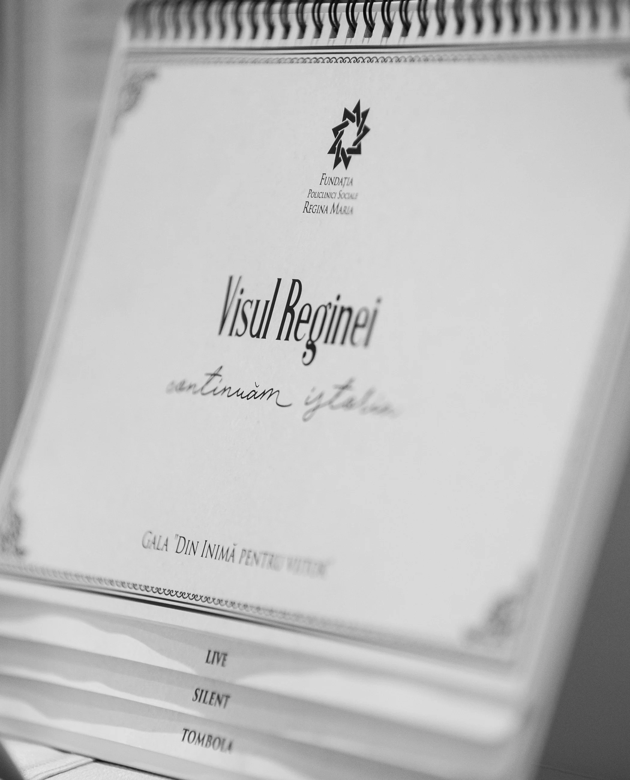 Black and white photograph of a booklet or program with a spiral binding at the top, with the heading 'Visul Reînoire' and smaller text below, including words like 'LIVE', 'SILENT', and 'TOMBOLA'.
