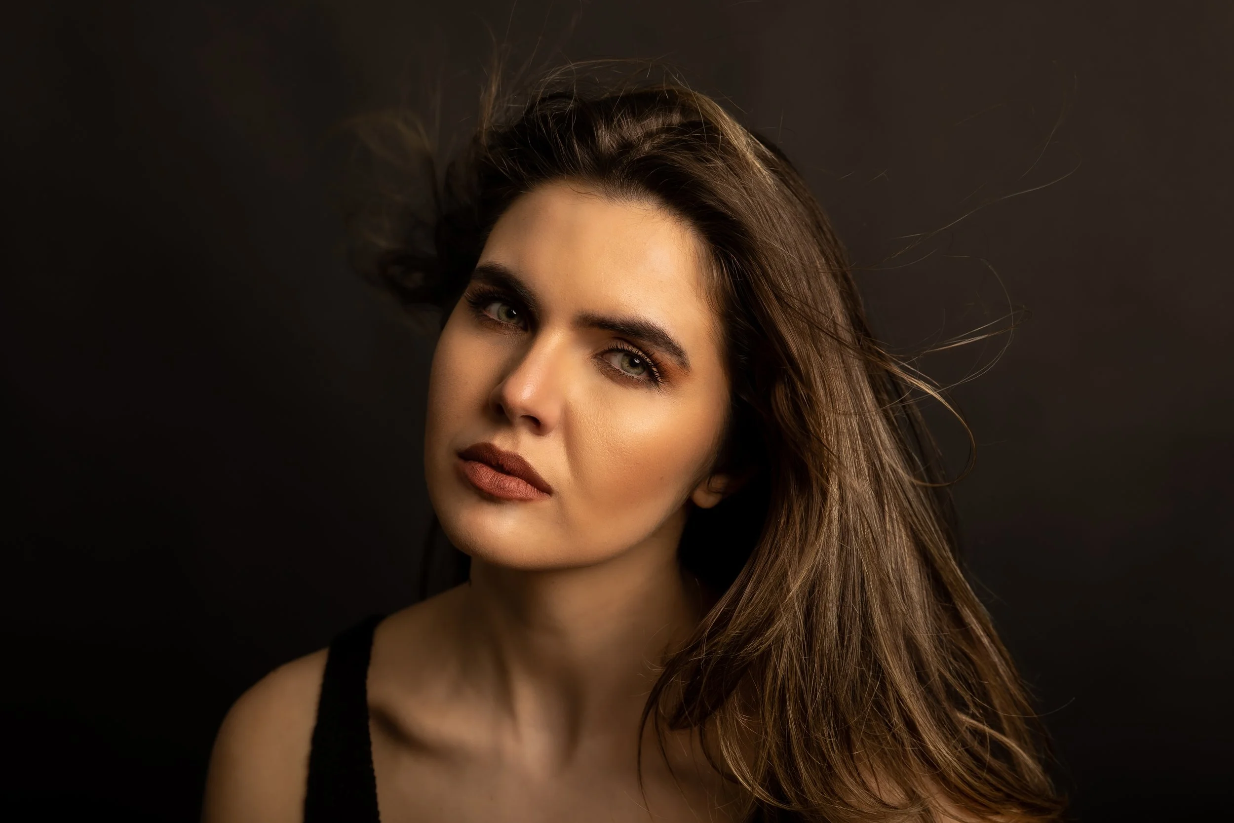 A woman with long brown hair and green eyes poses against a dark background.