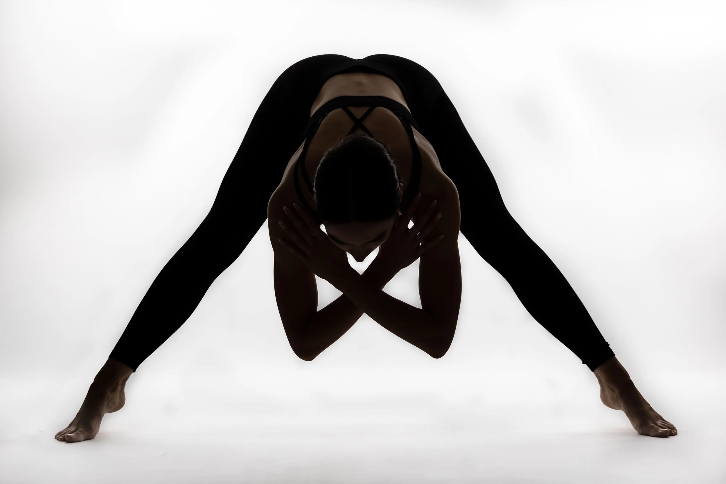 A person practicing yoga in a wide-legged Forward Bend position against a white background.