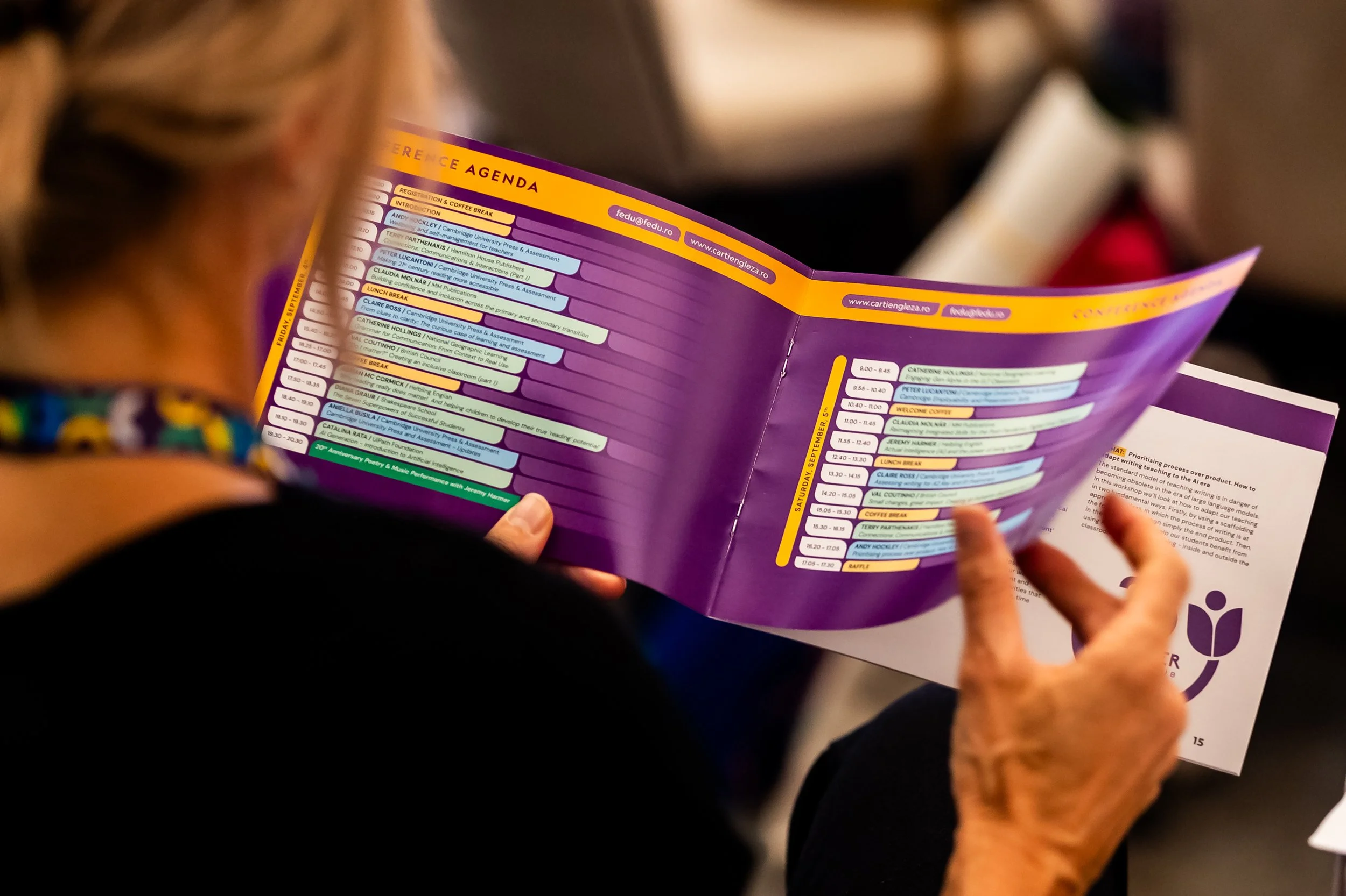 Close-up of a person holding a colorful event schedule in a brochure, with multiple name tags and schedule details visible on the pages.