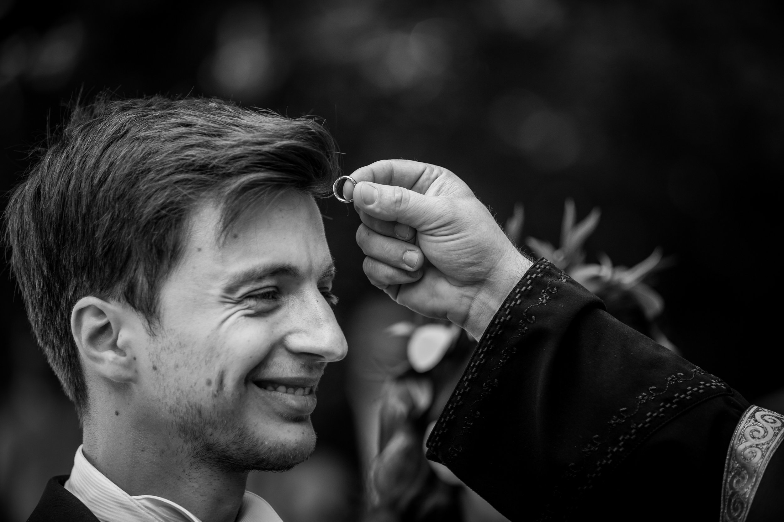 A person with short hair and earrings smiles as someone places a ring on their finger during a wedding ceremony.