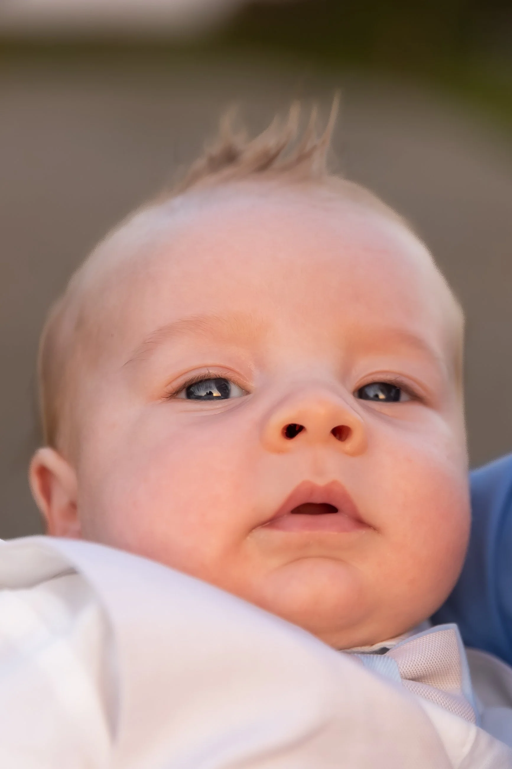Close-up of a baby's face with large eyes, chubby cheeks, and a small mouth, with part of their head and hair visible, lying on a blue surface.